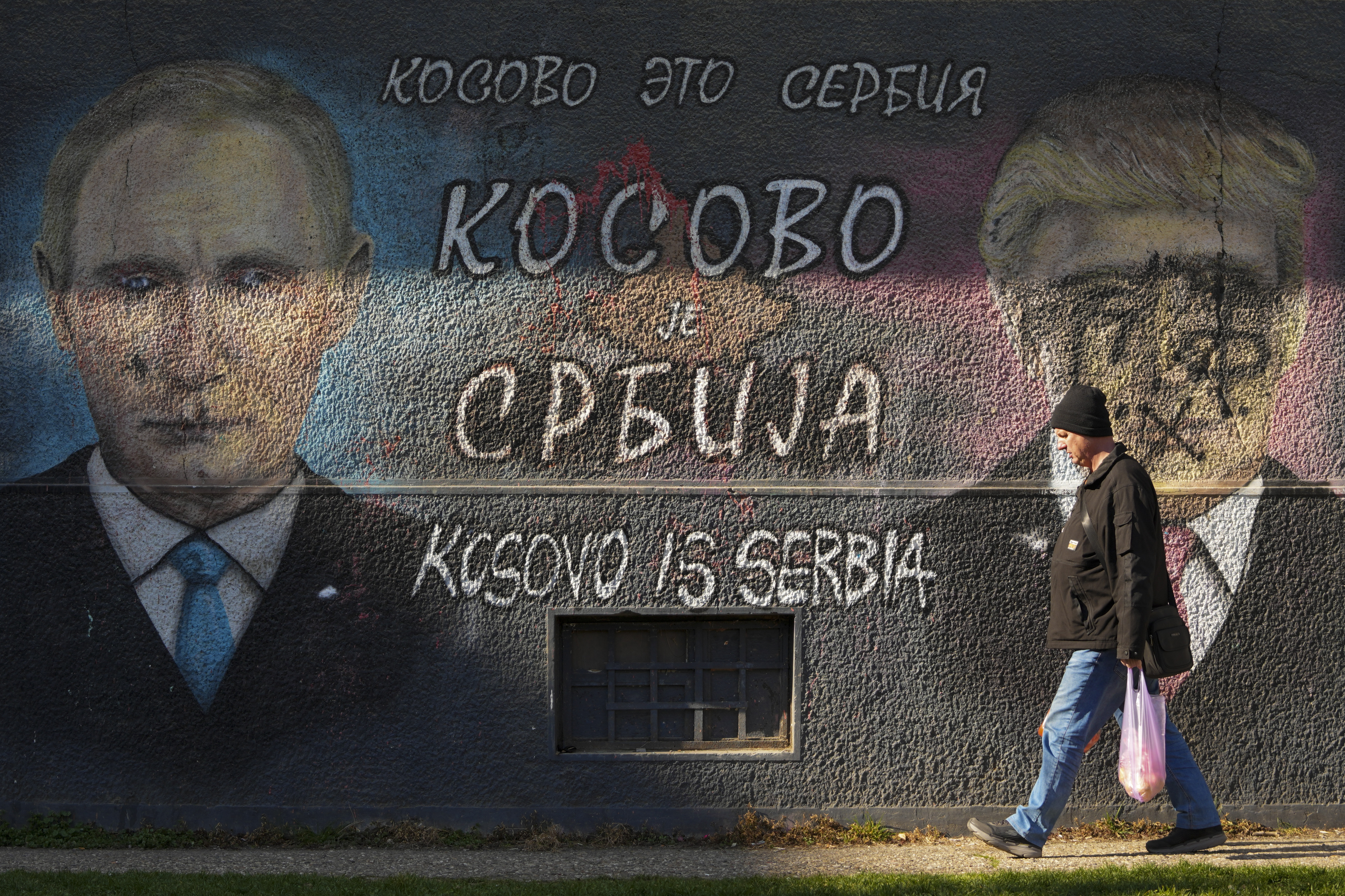 A man passes by a graffiti reading ''Kosovo is Serbia'' and depicting the Russian President Vladimir Putin, left, and U.S. President Donald Trump, vandalized with paint, in Belgrade, Serbia, Friday, Feb. 21, 2025. (AP Photo/Darko Vojinovic)