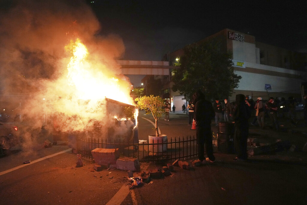 Protesters starts fire in the trash dumpster near the metropolitan detention center of downtown Los Angeles, Sunday, June 8, 2025. (AP Photo/Eric Thayer)