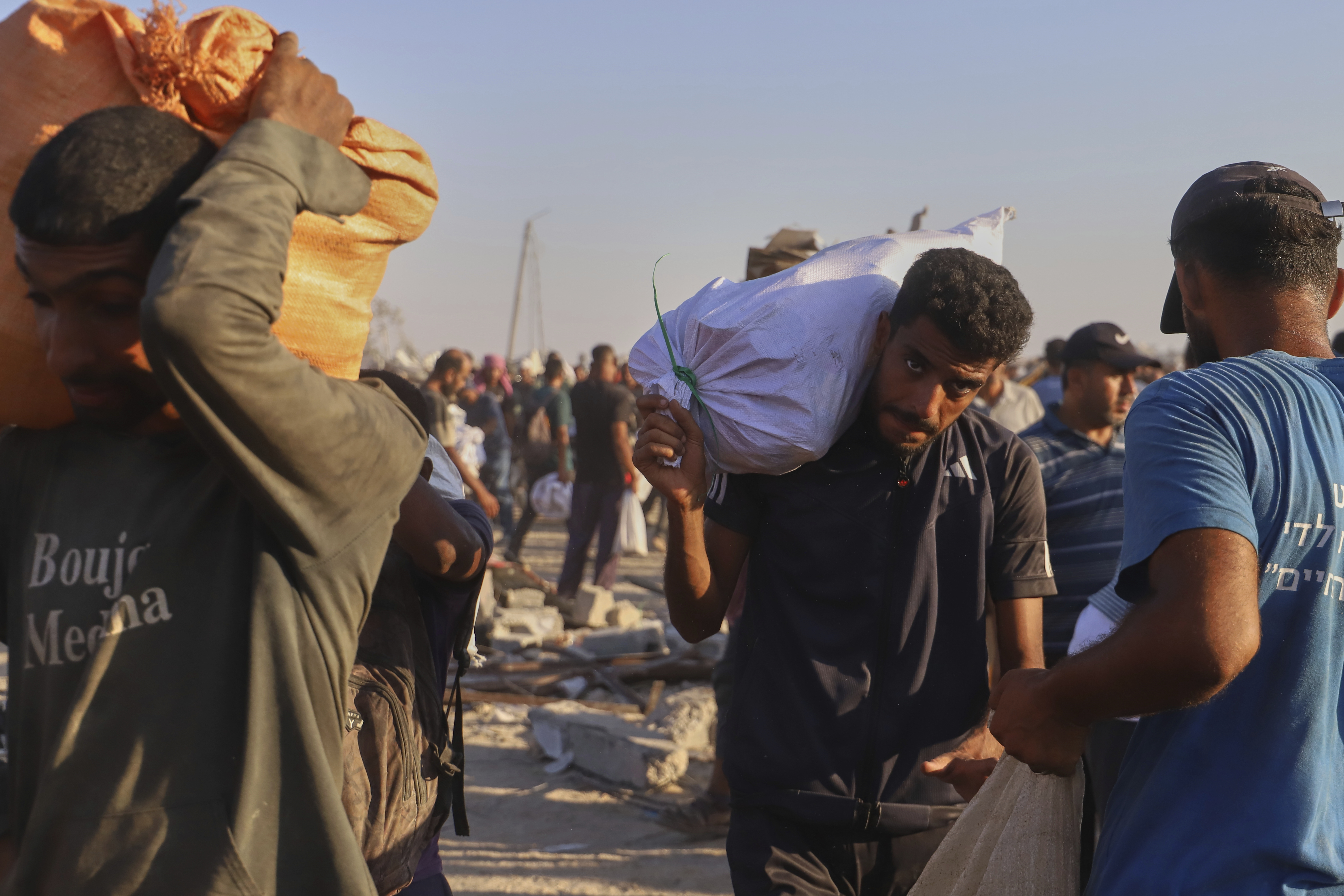 Palestinians carry packages of food taken from a humanitarian aid convoy that moved along the Morag corridor near Rafah, in the southern Gaza Strip, Monday, Aug. 4, 2025. (AP Photo/Mariam Dagga)