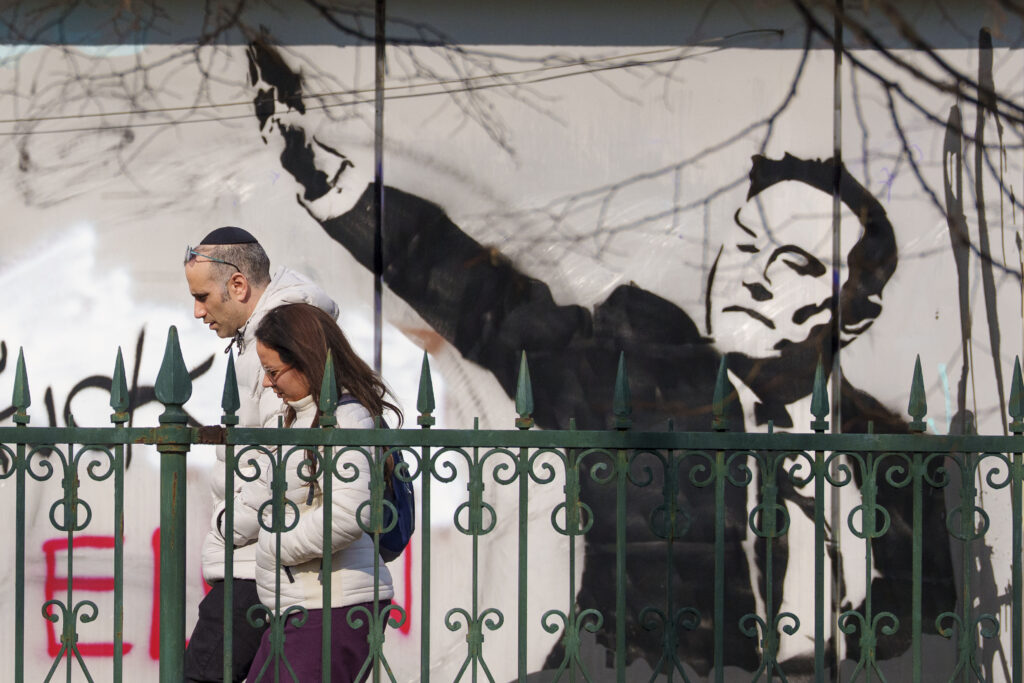 People walk by graffiti depicting Elon Musk, in Bucharest, Romania, Monday, March 3, 2025. (AP Photo/Andreea Alexandru)