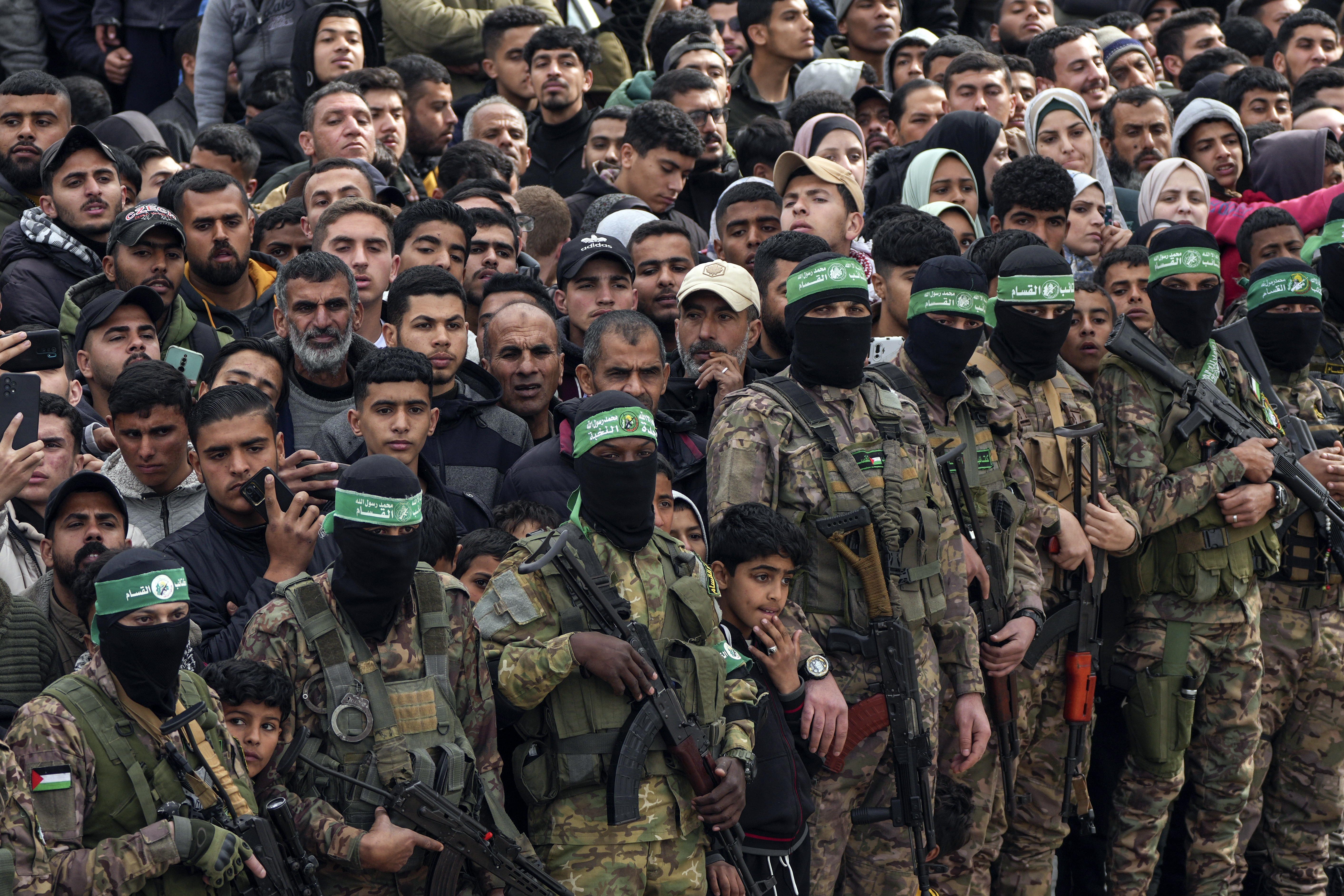 Palestinians watch as Hamas fighters stand in formation ahead of a hostages release in Deir al-Balah, central Gaza Strip, Saturday Feb. 8, 2025. (AP Photo/Abdel Kareem Hana)