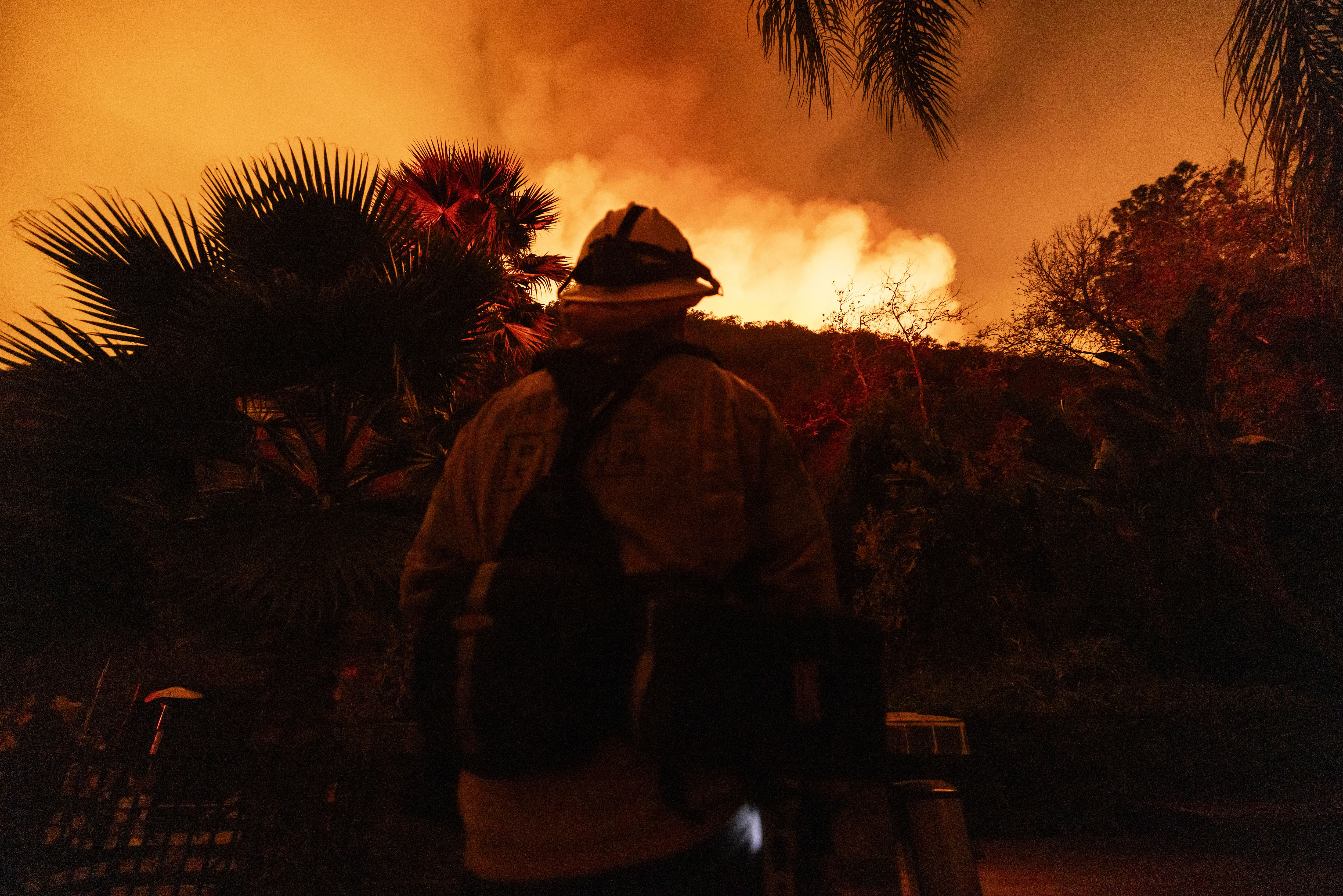 A firefighter looks at flames and smoke from the Palisades Fire as firefighters monitor the spread of the fire, in Mandeville Canyon, Saturday, Jan. 11, 2025, in Los Angeles. (AP Photo/Etienne Laurent)