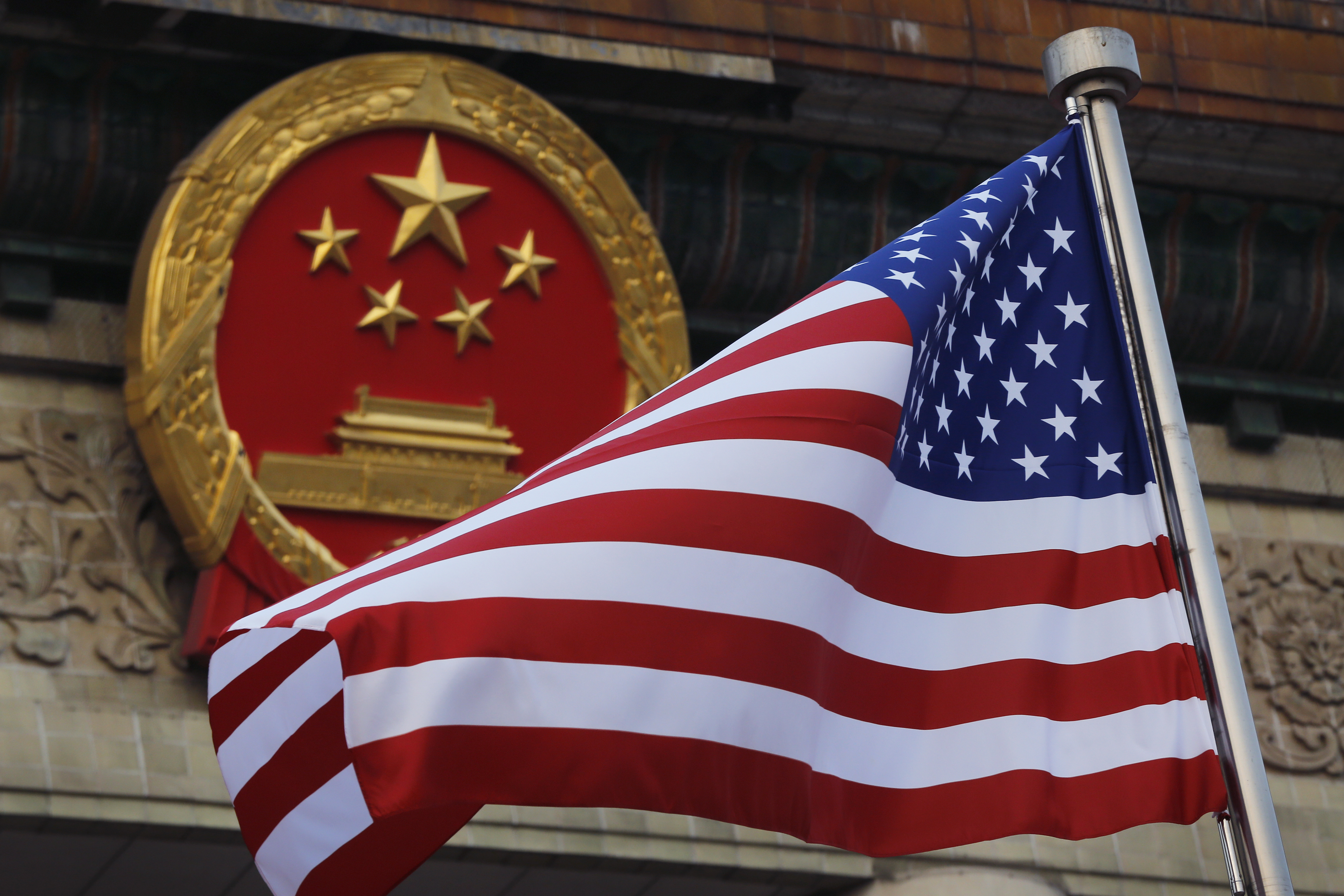FILE - An American flag is flown next to the Chinese national emblem outside the Great Hall of the People in Beijing, Nov. 9, 2017.  (AP Photo/Andy Wong, File)
