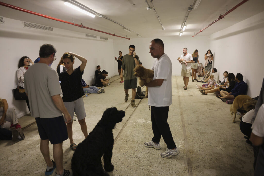 People take shelter as a siren sounds a warning following a missiles that were launched from Iran, in Tel Aviv, Israel, on Friday, June 13, 202 5. (AP Photo/Tomer Appelbaum)