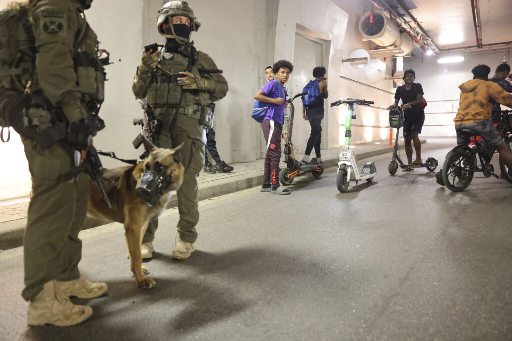 People and soldiers take cover as a siren sounds a warning following a missiles that were launched from Iran, in Tel Aviv, Israel, on Friday, June 13, 202 5. (AP Photo/Tomer Appelbaum)