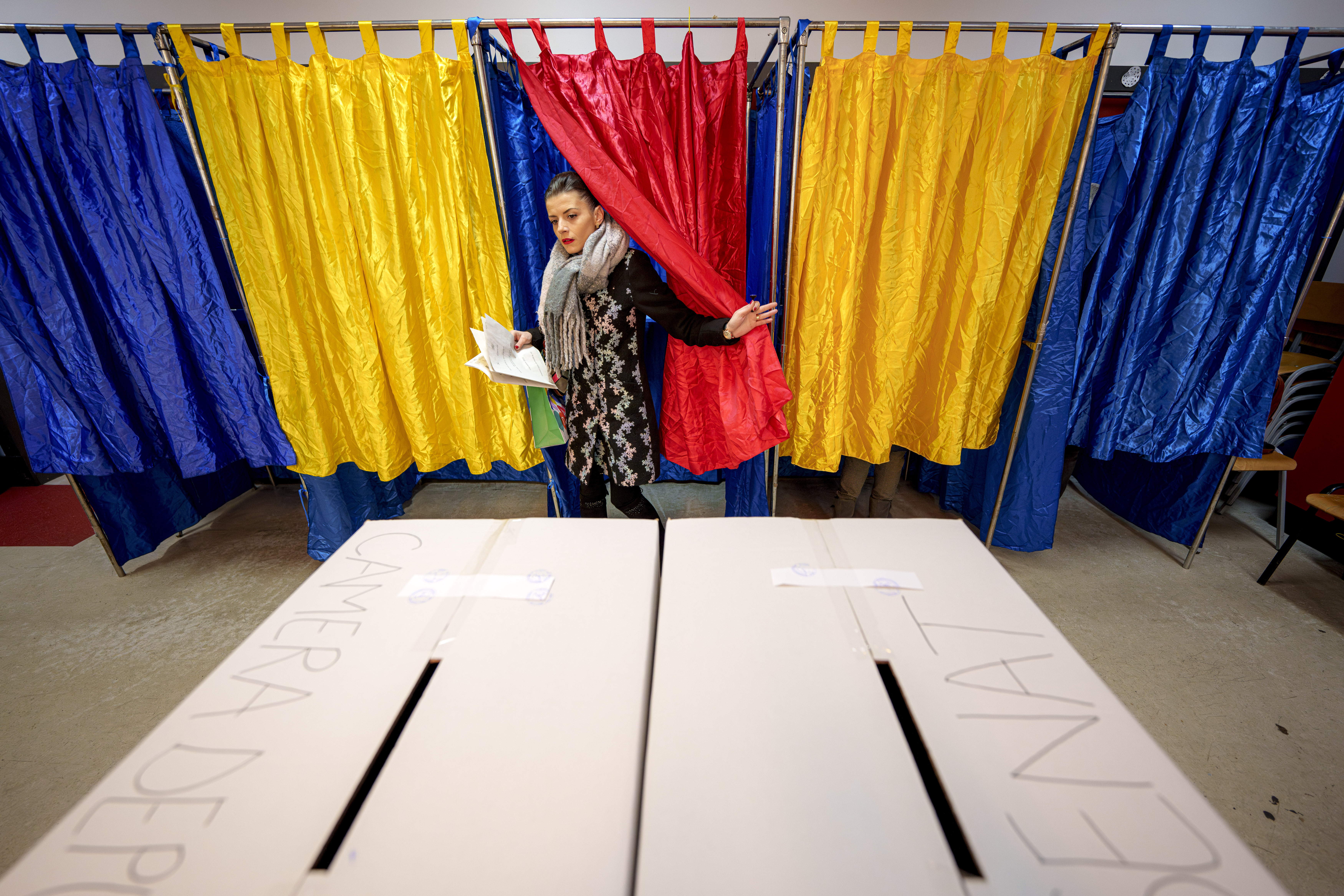 A woman exits a voting cabin with the colours of the Romanian flag as curtains before casting her vote in the country's parliamentary elections, in Bucharest, Romania, Sunday, Dec. 1, 2024. (AP Photo/Andreea Alexandru)