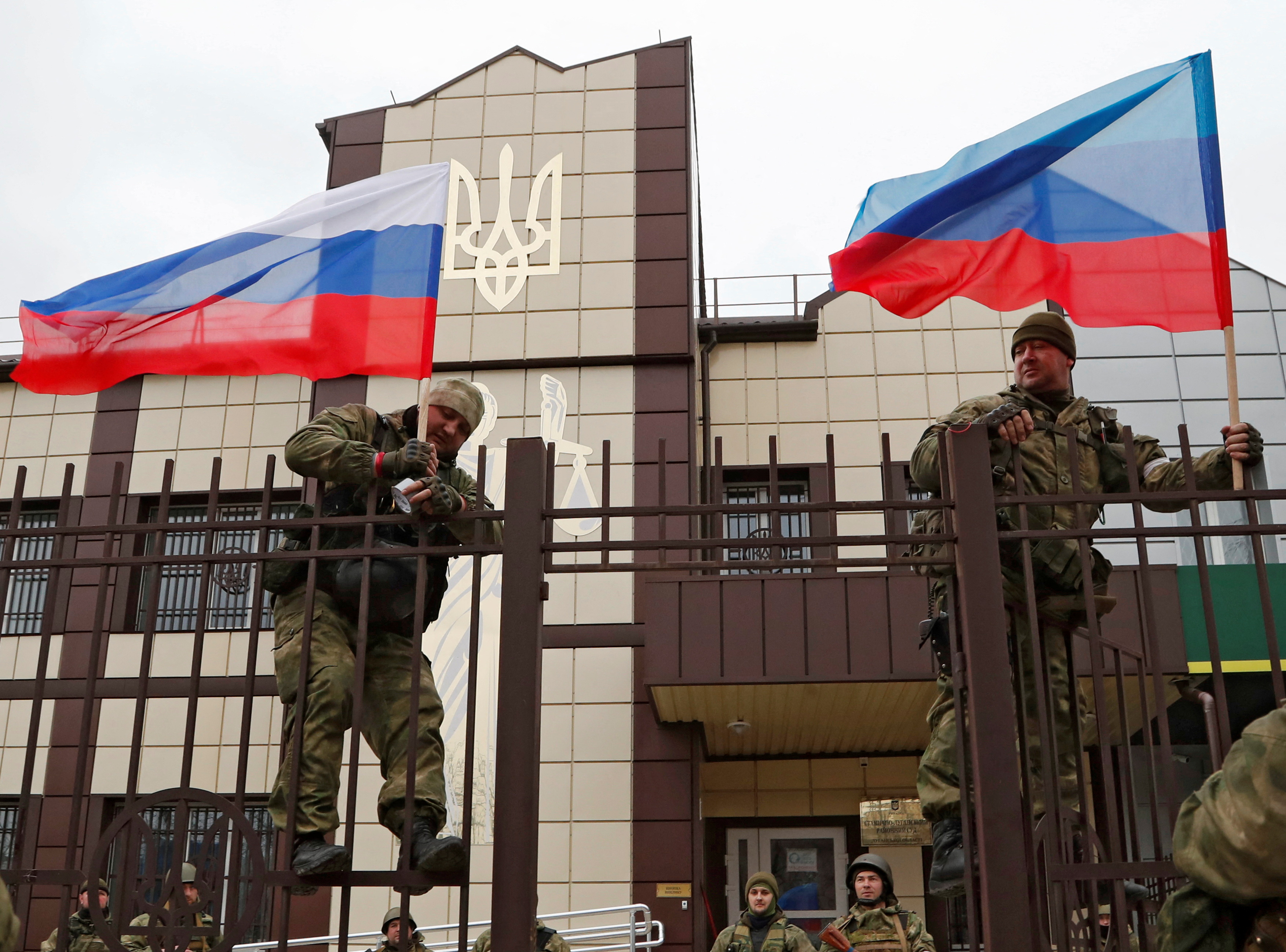 Servicemen of pro-Russian militia hoist flags of Russia and the separatist self-proclaimed Luhansk People's Republic (LNR) outside the Oschad bank branch in Stanytsia Luhanska in the Luhansk region, Ukraine February 27, 2022. REUTERS/Alexander Ermochenko