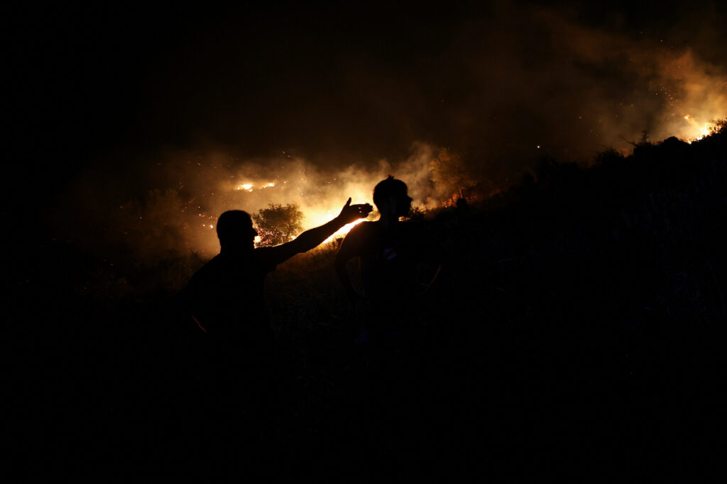 People stand near a wildfire as firefighters and locals work to contain it near Qeparo, Albania, August 19, 2023. REUTERS/Florion Goga