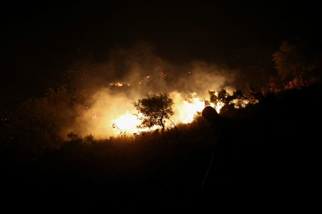 A person stands near a wildfire as firefighters and locals work to contain it near Qeparo, Albania, August 19, 2023. REUTERS/Florion Goga