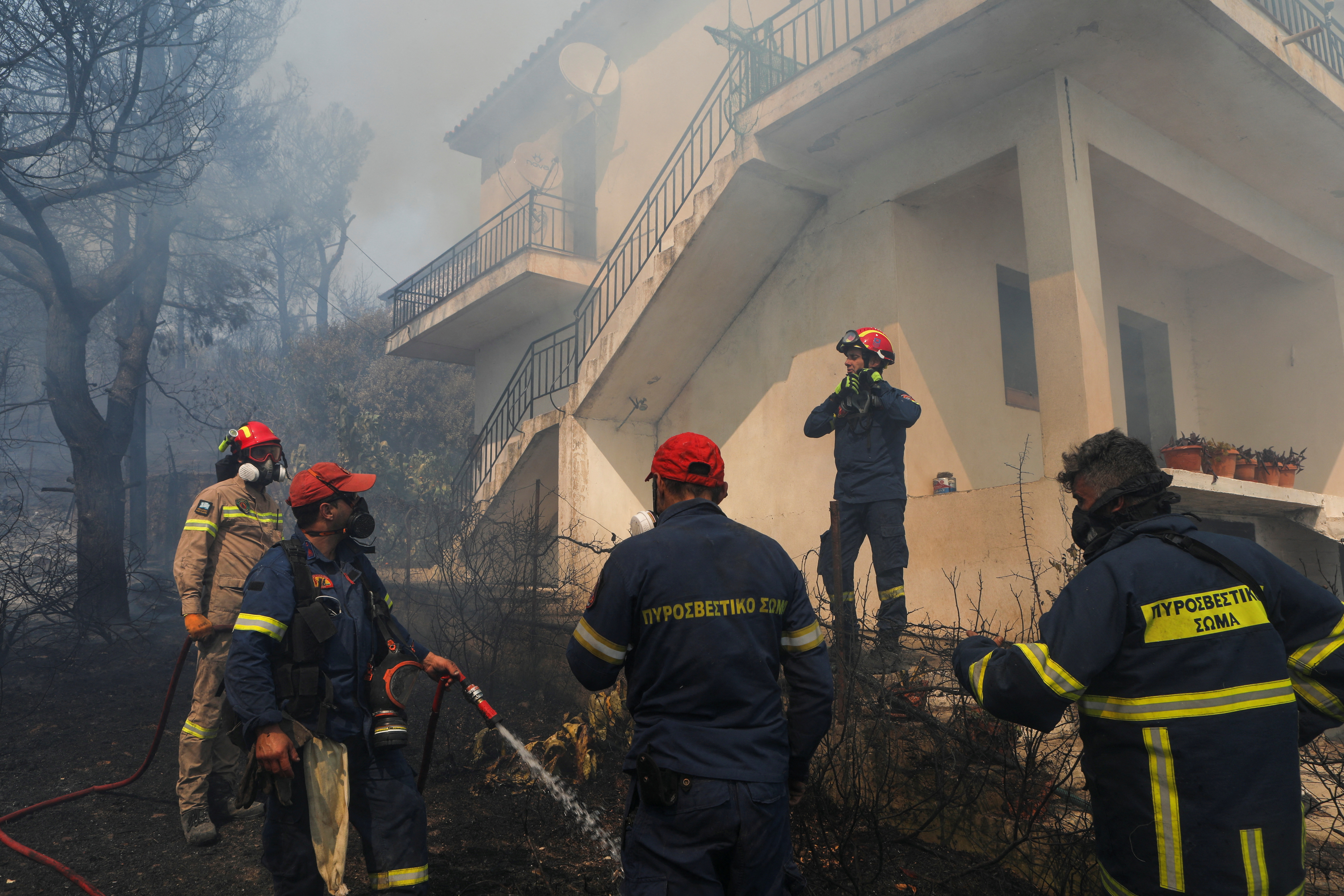 Firefighters prepare to extinguish a fire in a house as a wildfire rages at the village of Vatera, on the island of Lesbos, Greece July 23, 2022. REUTERS/Elias Marcou
