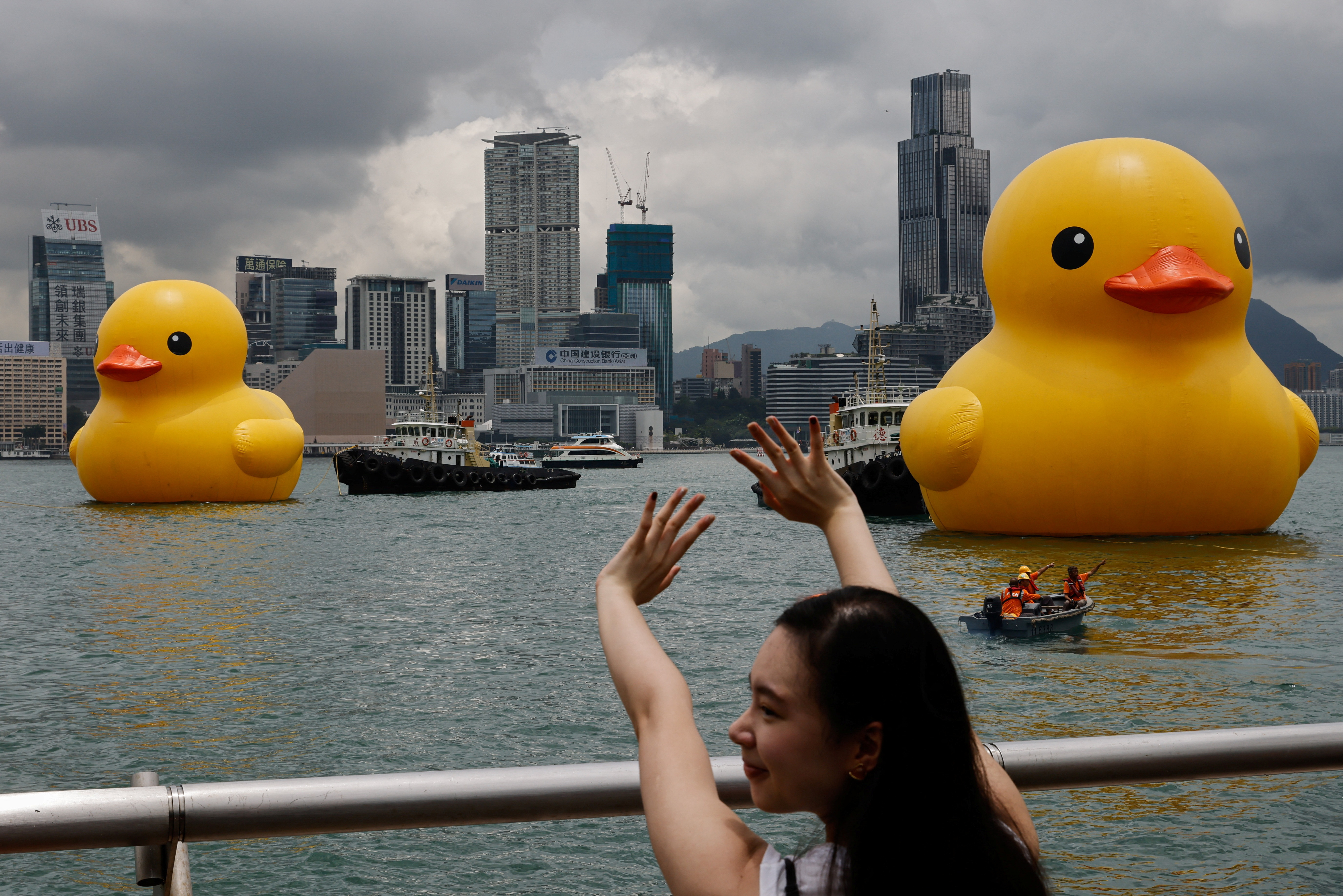 A woman poses for a photo as an art installation, dubbed "Double Ducks" by Dutch artist Florentijn Hofman, is seen in the background at Victoria Harbour, in Hong Kong, China June 9, 2023. REUTERS/Tyrone Siu