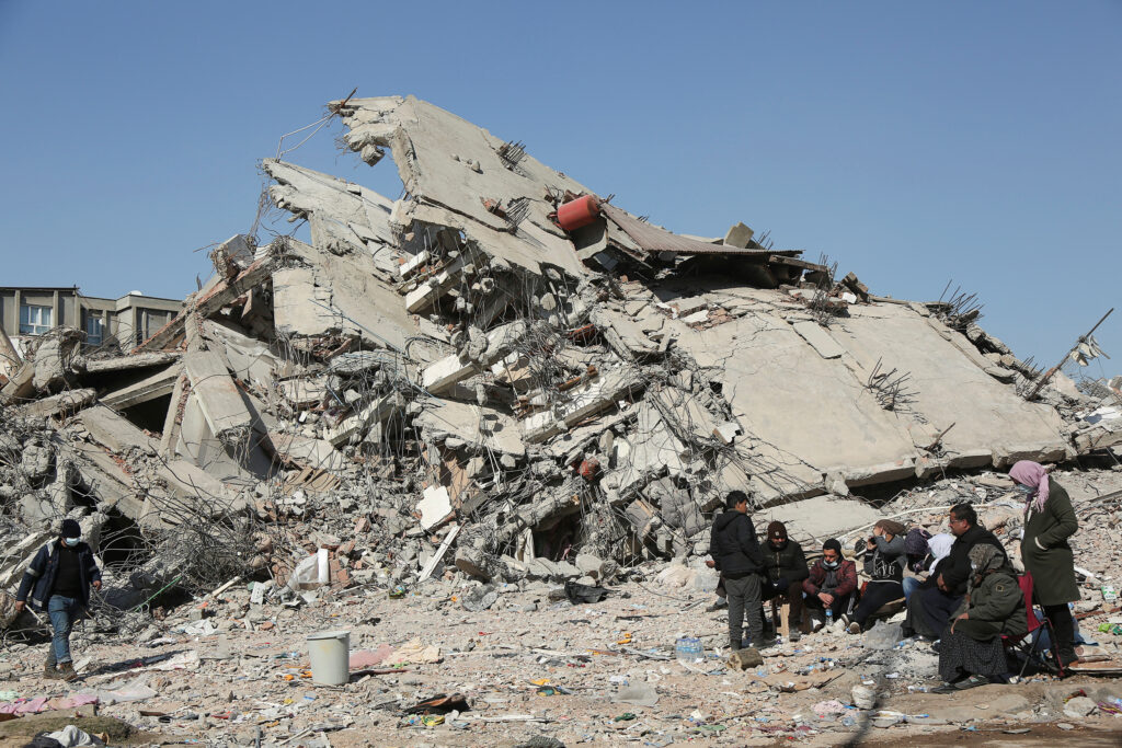 People sit and stand near a collapsed building, in the aftermath of the deadly earthquake, in Adiyaman, Turkey, February 12, 2023. REUTERS/Sertac Kayar