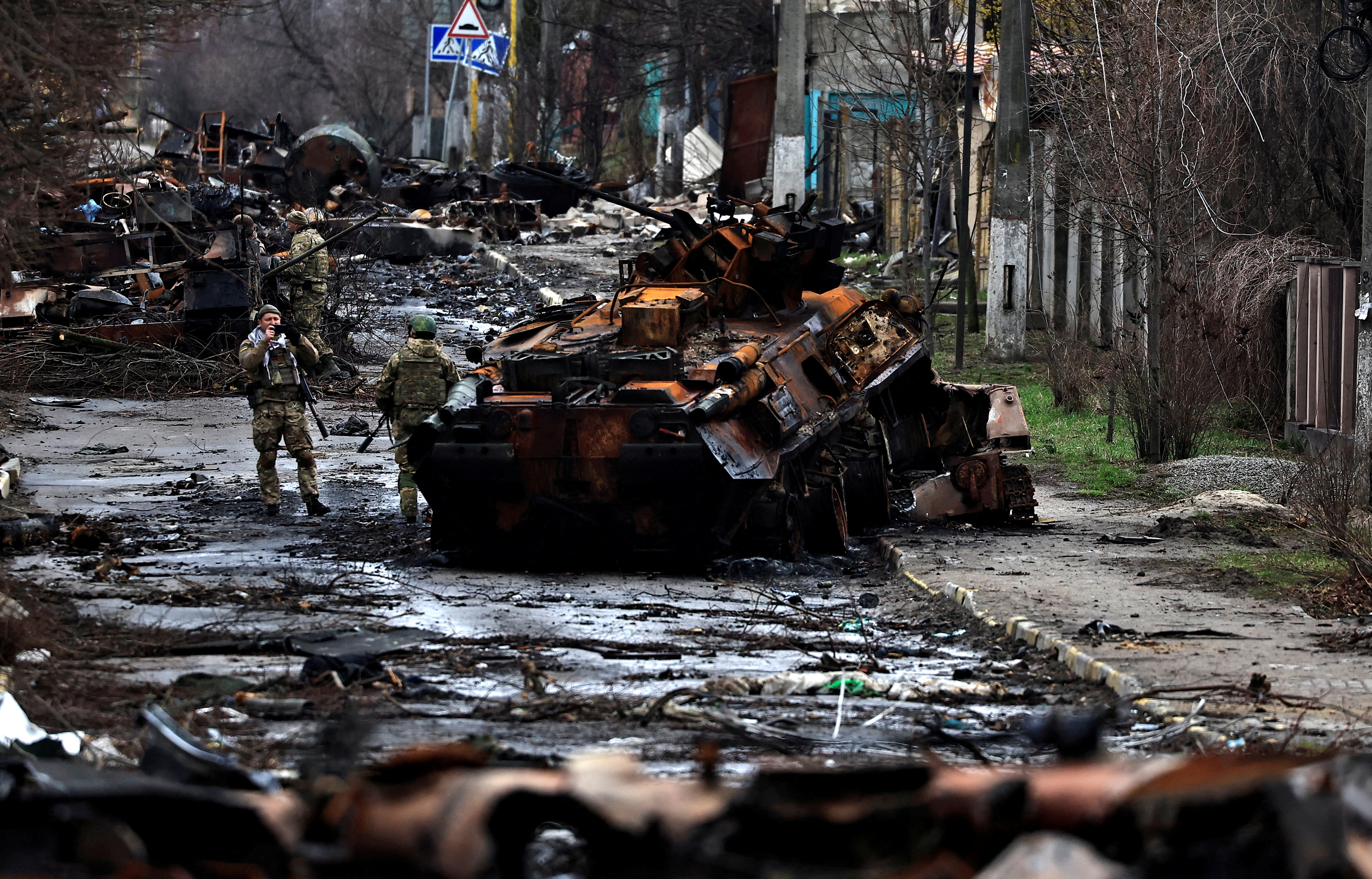 A soldier takes a photograph of his comrade as he poses beside a destroyed Russian tank and armoured vehicles, amid Russia's invasion on Ukraine, in Bucha, in Kyiv region