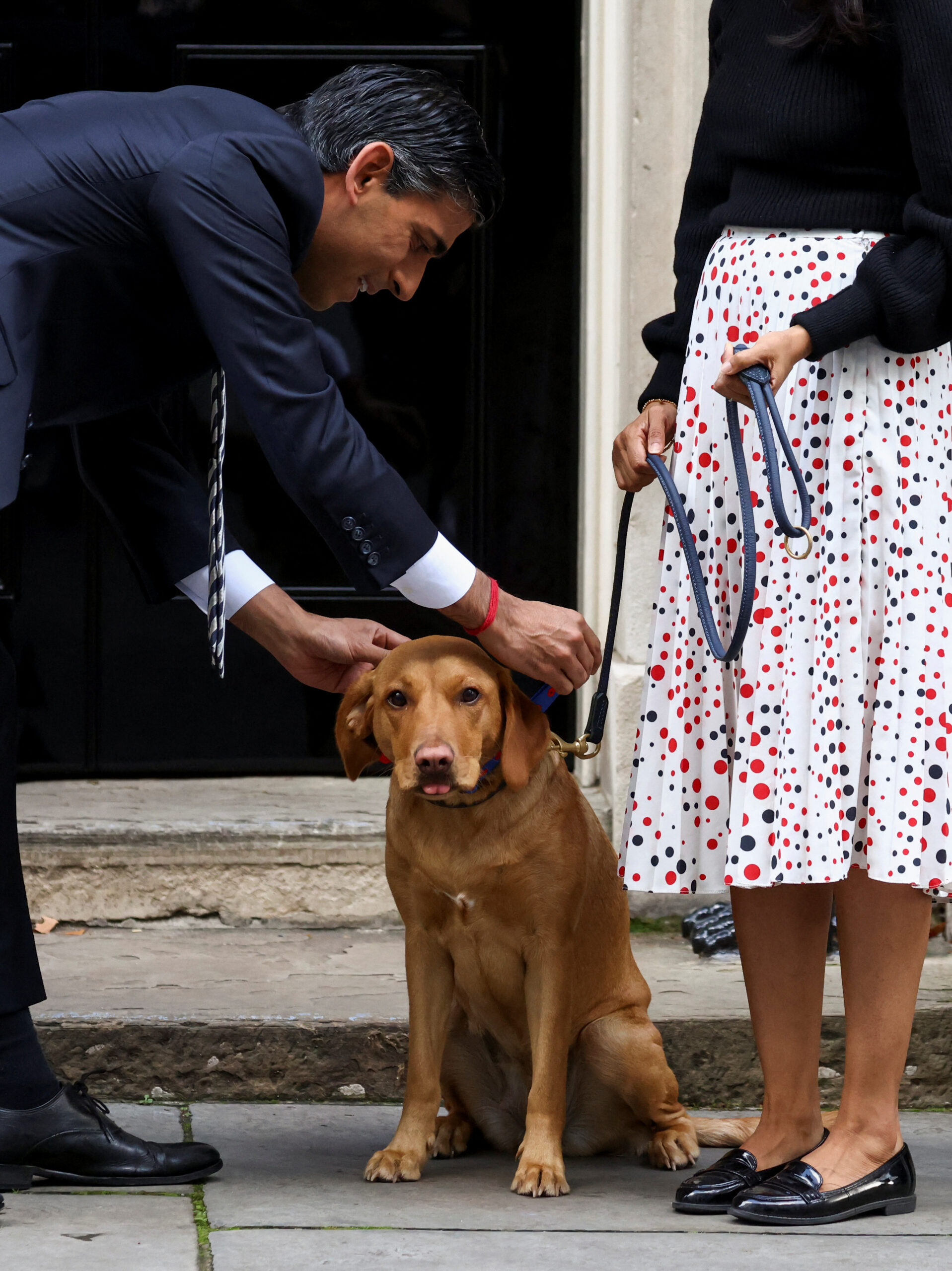 British Prime Minister Rishi Sunak tends to his dog Nova, next to his wife Akshata Murty, as they meet volunteers from the Royal British Legion outside Number 10 Downing Street in London, Britain, October 31, 2022. REUTERS/Henry Nicholls