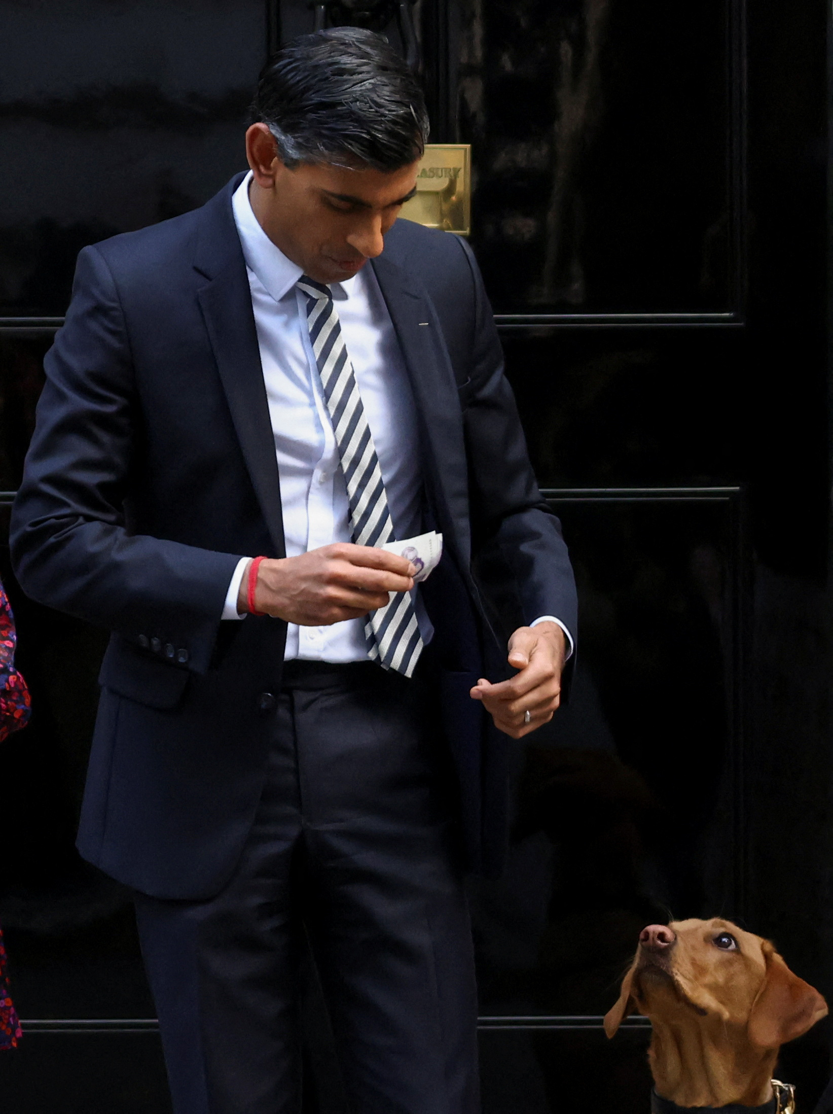 British Prime Minister Rishi Sunak holds money to purchase a poppy pin from Royal British Legion fundraisers, next to his dog Nova, as he meets them outside Number 10 Downing Street in London, Britain, October 31, 2022. REUTERS/Henry Nicholls