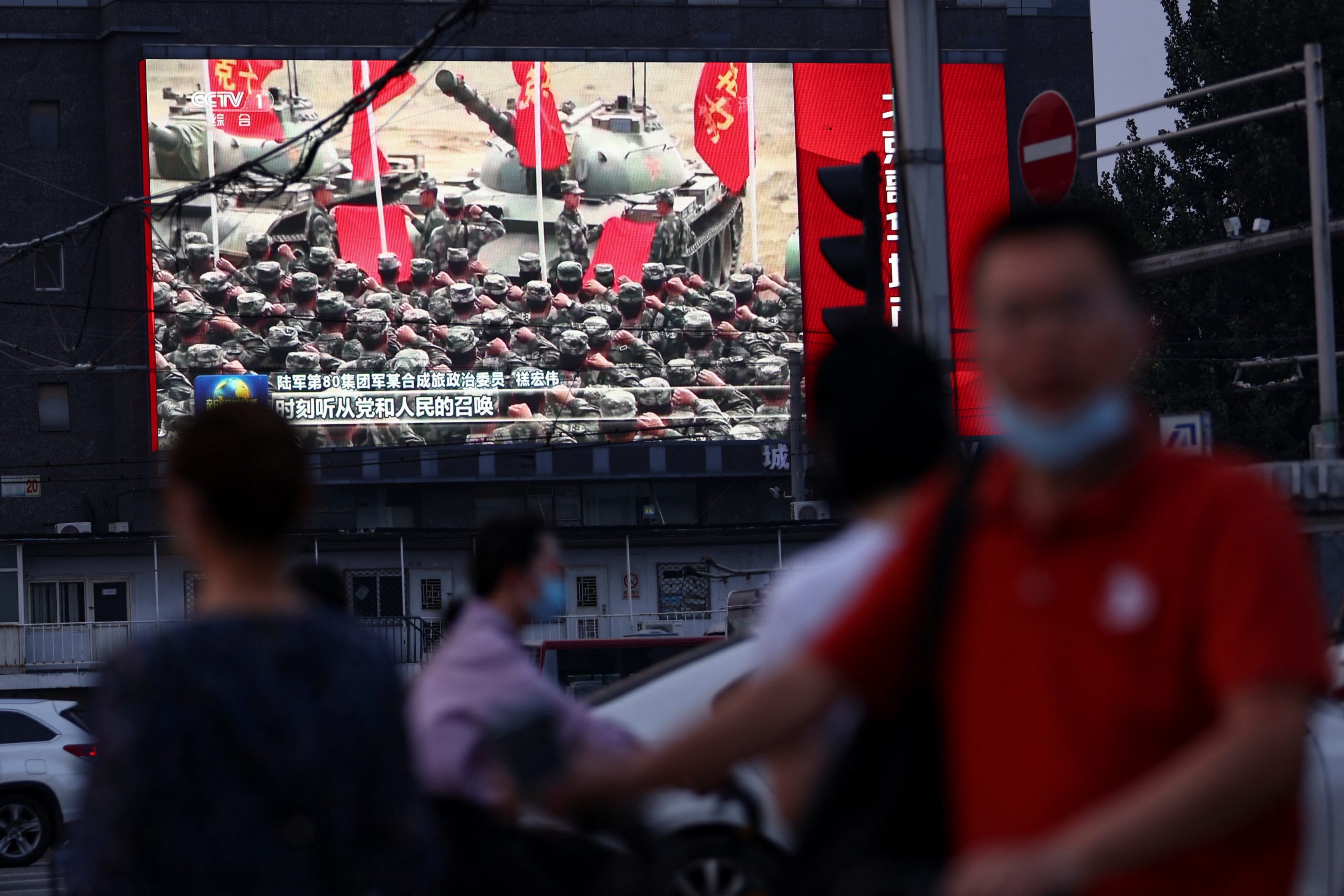 Pedestrians walk past a screen showing footage of Chinese People's Liberation Army (PLA) soldiers during an evening news programme, in Beijing, China August 2, 2022. REUTERS/Tingshu Wang