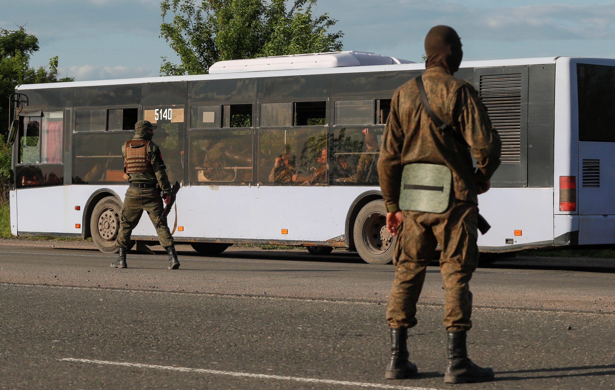 Service members of pro-Russian troops guard a road near a bus carrying Ukrainian soldiers, who surrendered at the besieged Azovstal steel mill in the course of Ukraine-Russia conflict, outside Mariupol, Ukraine May 20, 2022. REUTERS/Alexander Ermochenko