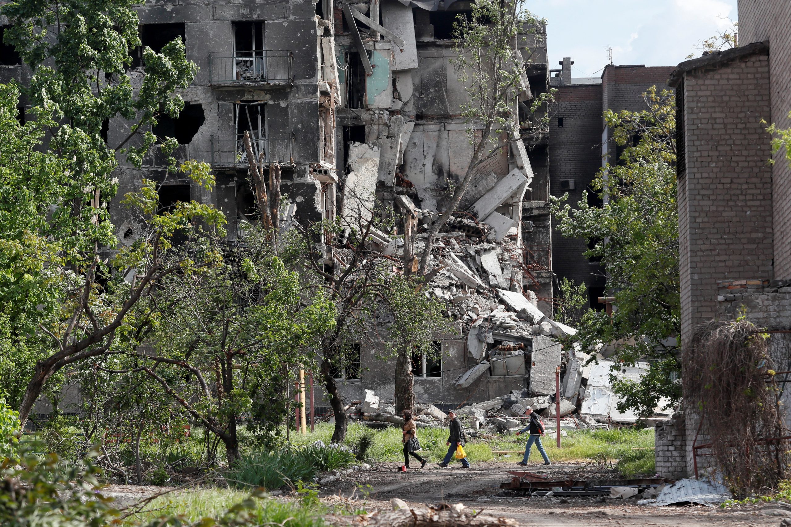 People walk past a residential building heavily damaged during Ukraine-Russia conflict in the southern port city of Mariupol, Ukraine May 15, 2022. REUTERS/Alexander Ermochenko