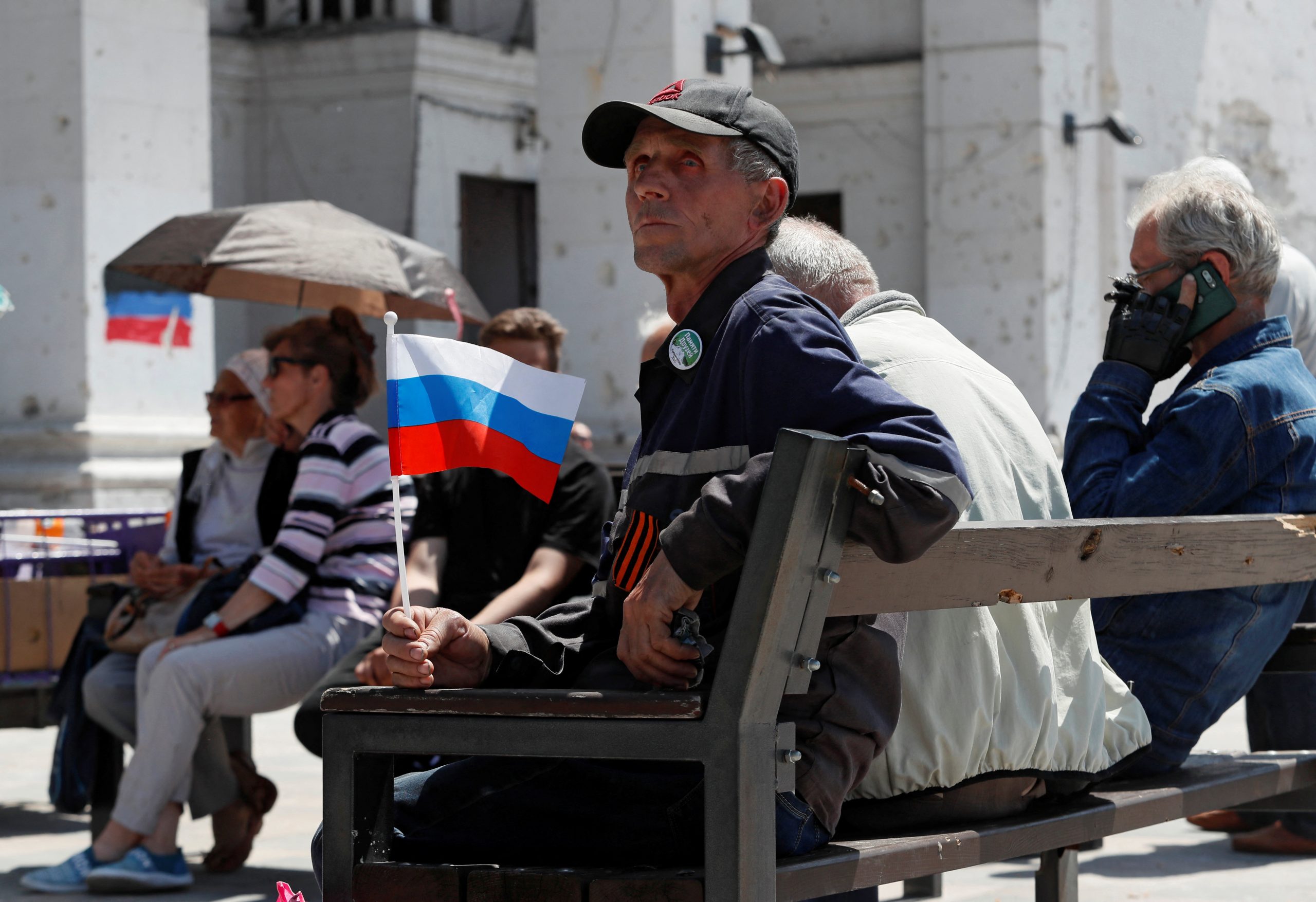 A man holds a Russian flag as he sits in front of a theatre building destroyed during Ukraine-Russia conflict in the southern port city of Mariupol, Ukraine May 30, 2022. REUTERS/Alexander Ermochenko