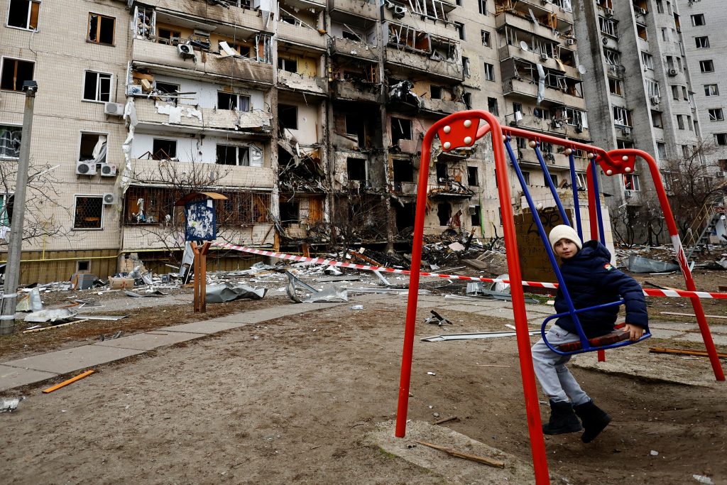 A child sits on a swing in front of a damaged residential building, after Russia launched a massive military operation against Ukraine, in Kyiv, Ukraine February 25, 2022. REUTERS/Umit Bektas