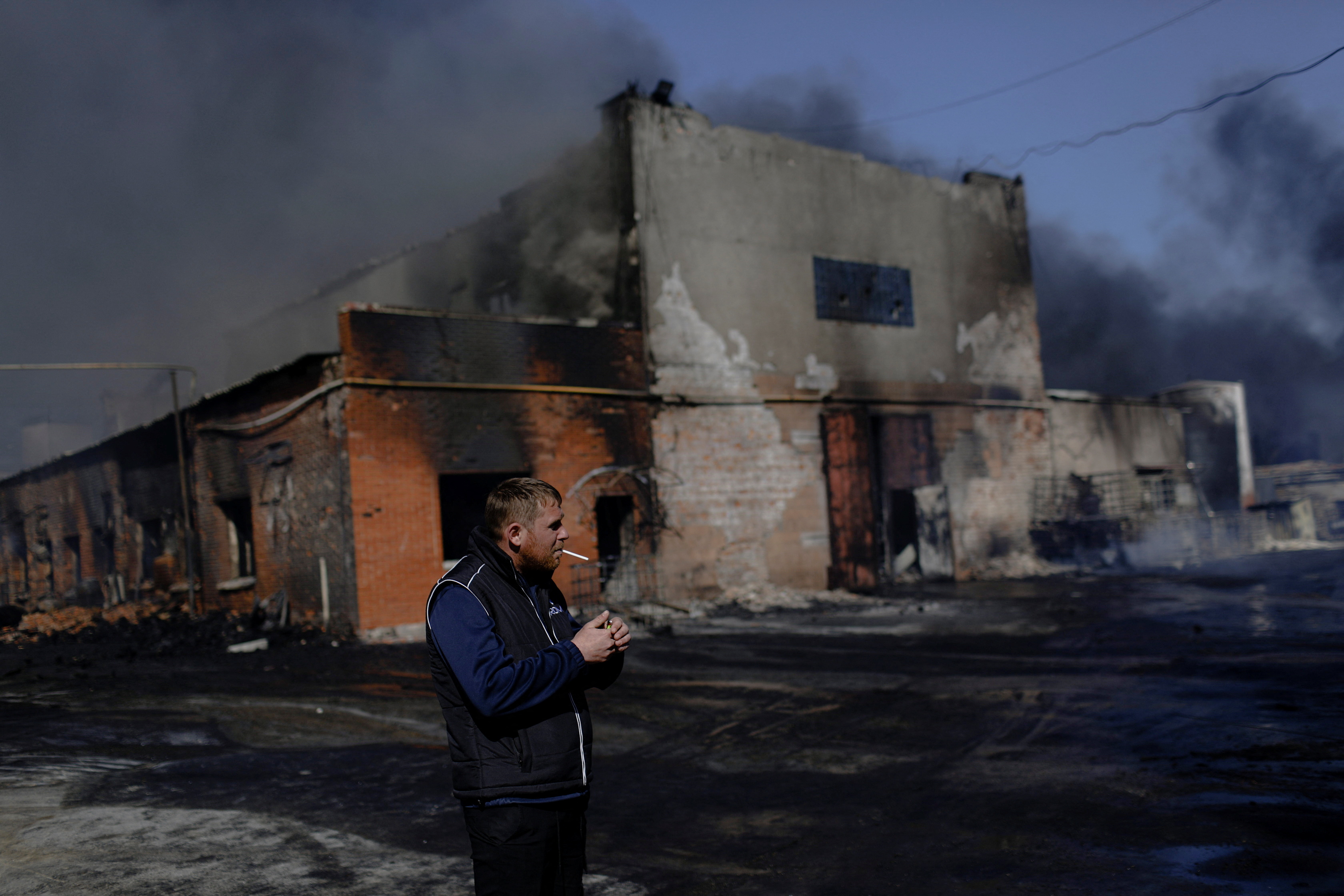 A man smokes outside a burning plant, following Russian shelling amid Russia's attack on Ukraine, in Kharkiv, Ukraine, April 30, 2022. REUTERS/Ricardo Moraes