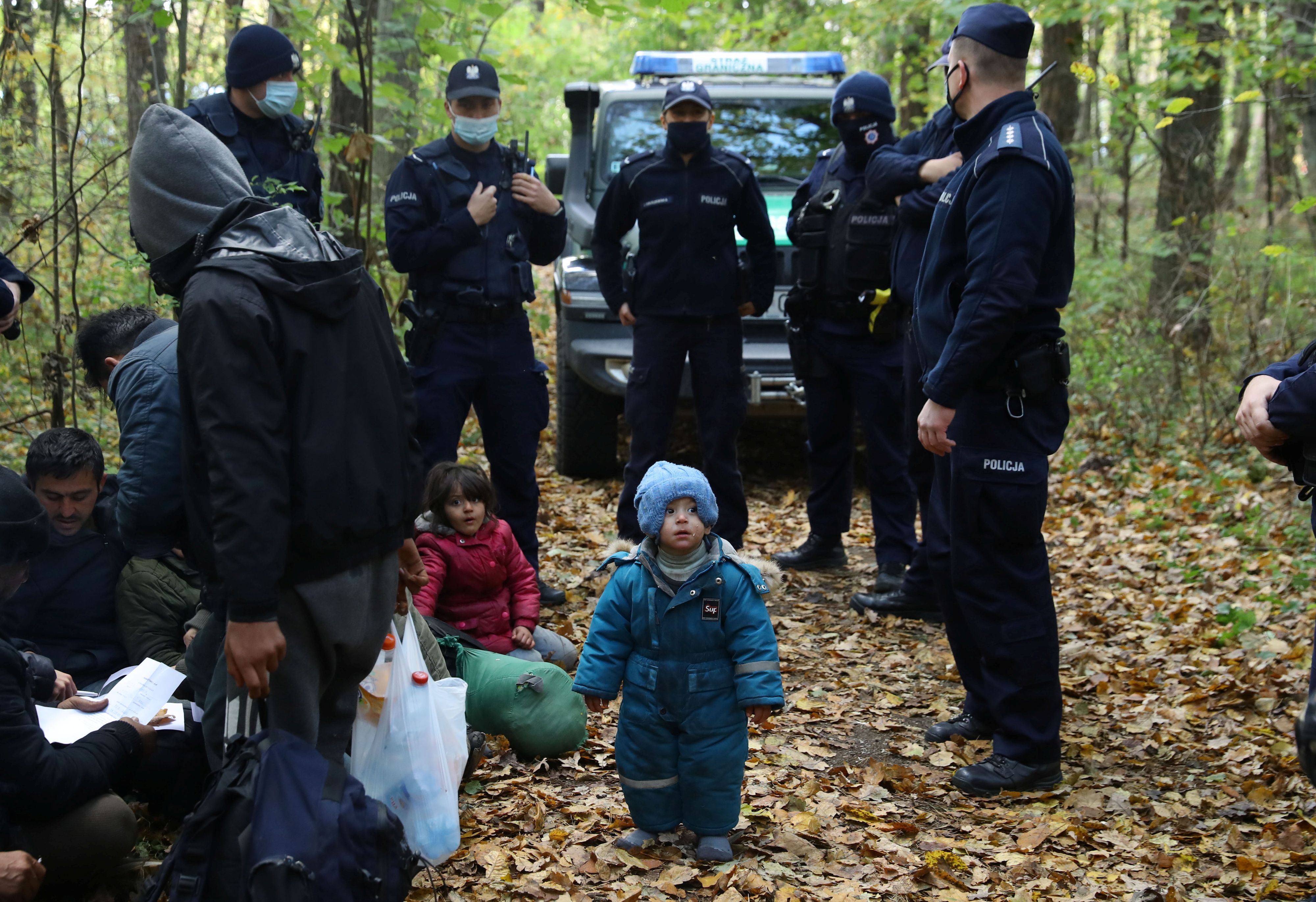 An Iraqi migrant child stands as he and others are surrounded by border guards and police officers after they crossed the Belarusian-Polish border during the ongoing migrant crisis, in Hajnowka