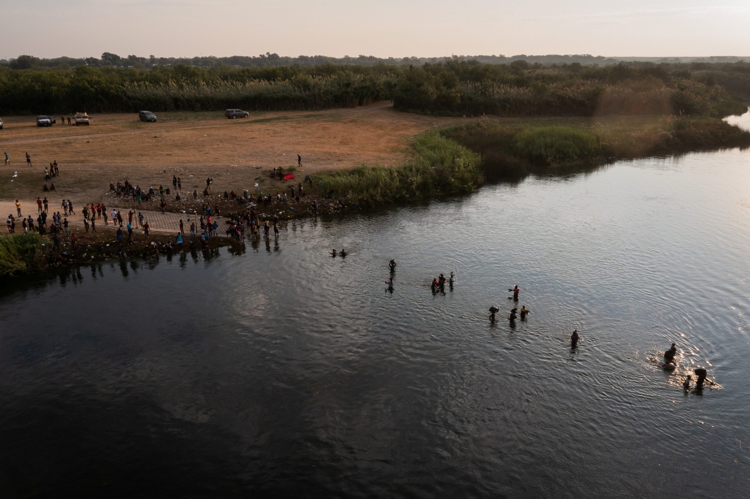 Migrants seeking refuge in the United States cross the Rio Grande river, with bags and children in tow, back into Ciudad Acuna, Mexico from their camp in Del Rio, Texas, U.S. September 21, 2021. Picture taken with a drone. REUTERS/Adrees Latif