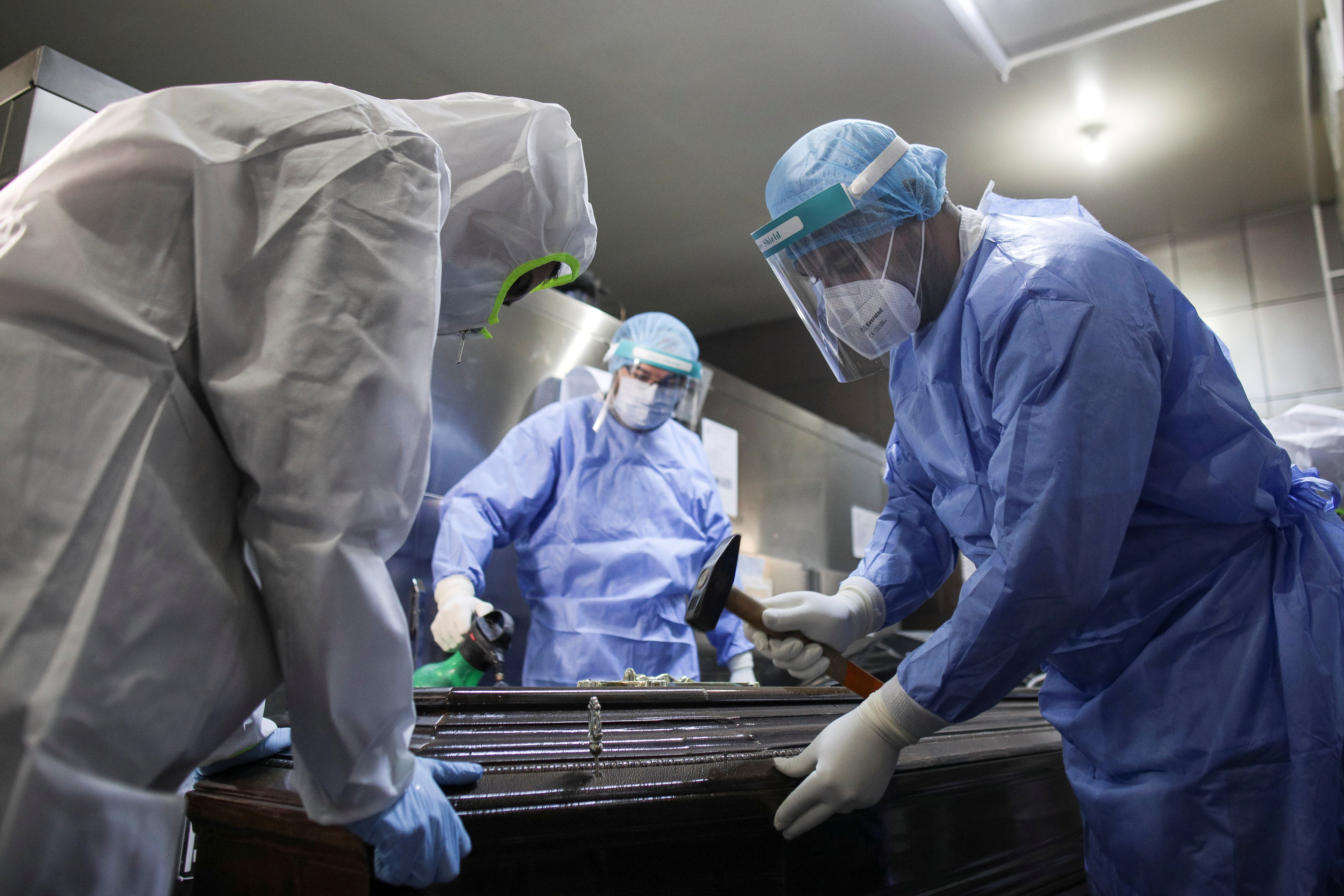 A nurse from Bucharest University Hospital morgue nails a coffin shut while preparing a COVID-19 victim for transport to a cemetery, in Bucharest