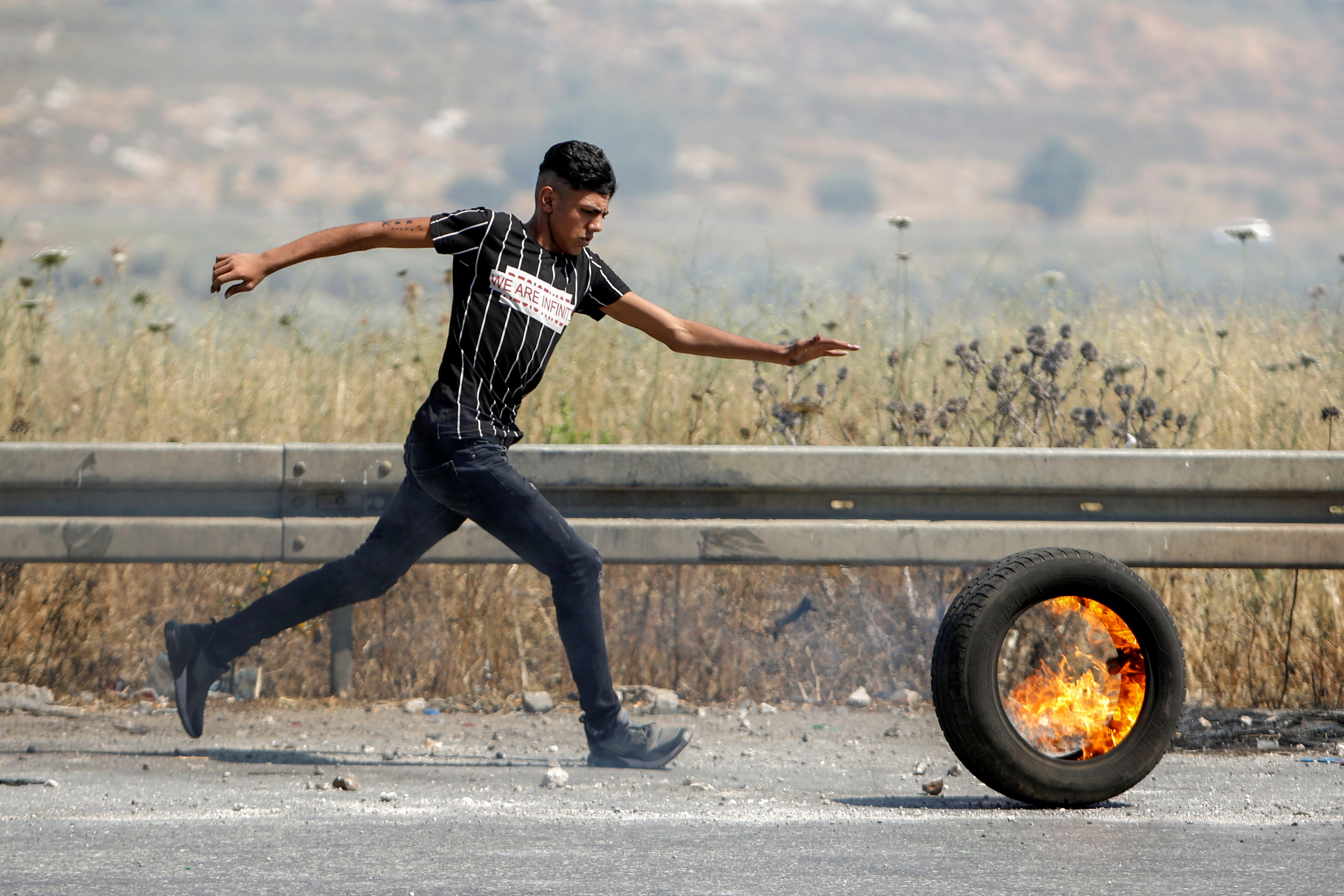 A Palestinian demonstrator rolls a burning tire during a protest over tension in Jerusalem and Israel-Gaza escalation, near Israel's Hawara checkpoint near Nablus in the Israeli-occupied West Bank, May 14, 2021. REUTERS/Raneen Sawafta