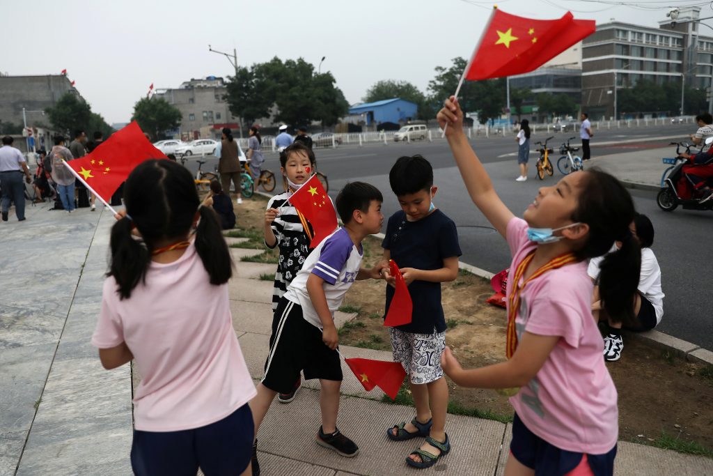 Children wave Chinese national flags on the street ahead of a rehearsal for the celebrations to mark the 100th founding anniversary of the Communist Party of China, in Beijing, China June 26, 2021. Picture taken June 26, 2021. REUTERS/Tingshu Wang