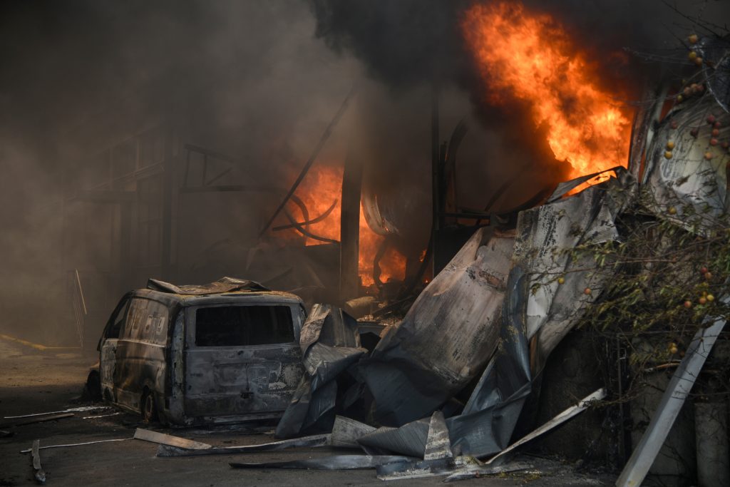 A burnt vehicle is seen as smoke and flames rise during a wildfire near the village of Afidnes, north of Athens, Greece, August 6, 2021. REUTERS/Alexandros Avramidis