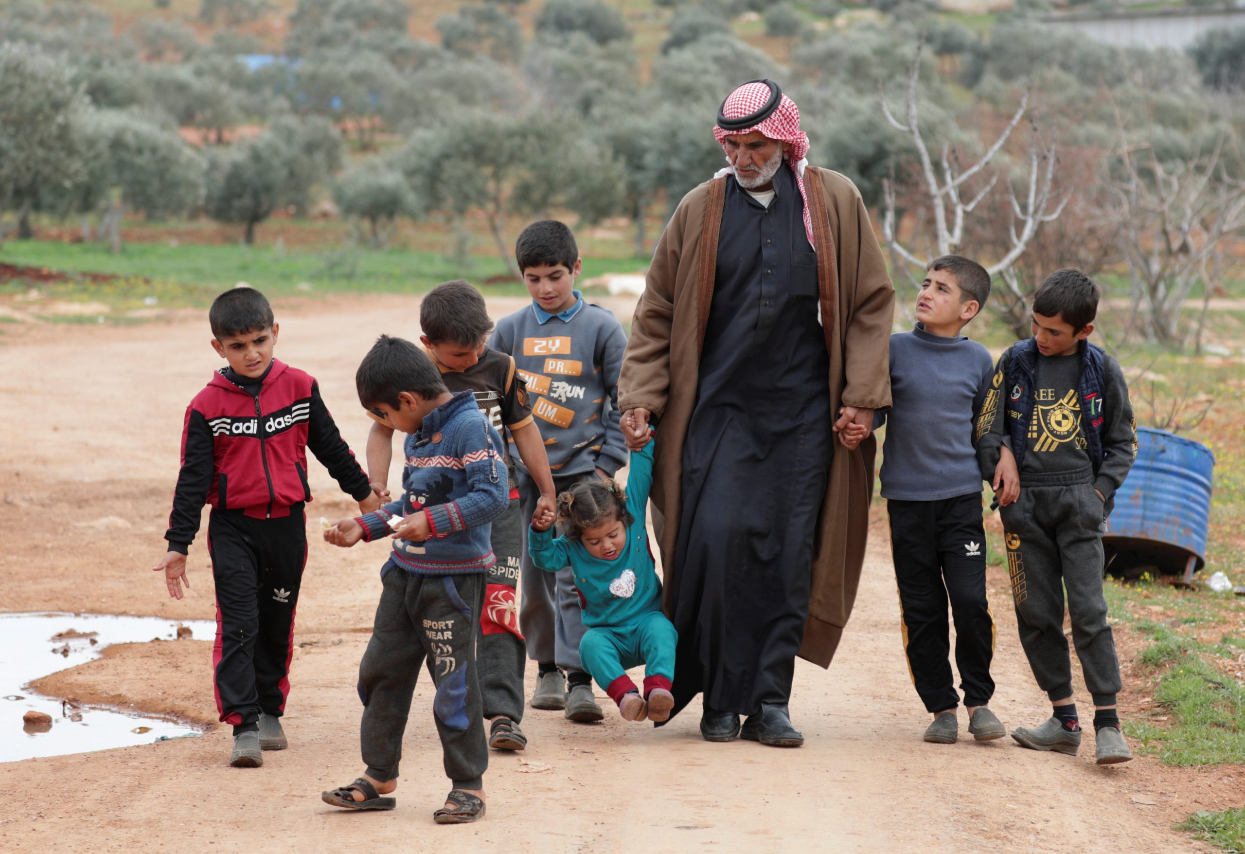 Abdel Razzak al-Khatoun, 84, a Syrian farmer, walks with his grandchildren, at an internally displaced camp in northern Idlib, Syria March 11, 2021. Picture taken March 11, 2021. REUTERS/Khalil Ashawi