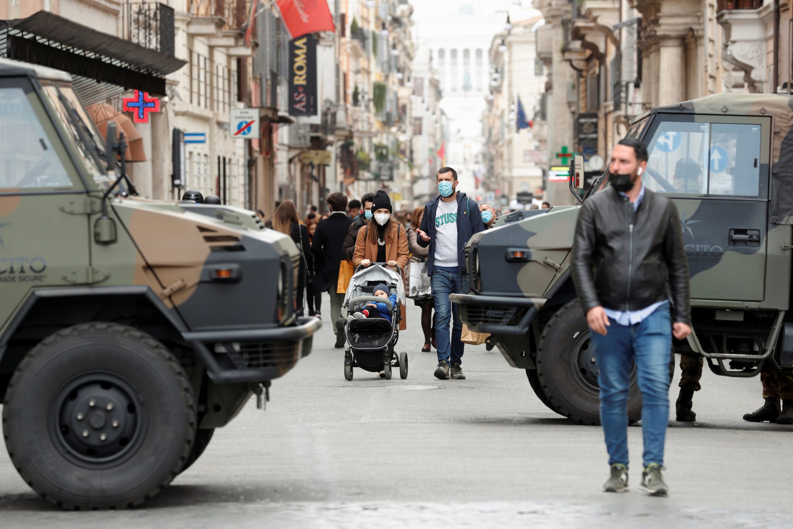 People walk past army vehicles at a street on the final day of open restaurants and bars before tighter coronavirus disease (COVID-19) restrictions are enforced, in Rome, Italy, March 14, 2021. REUTERS/Remo Casilli