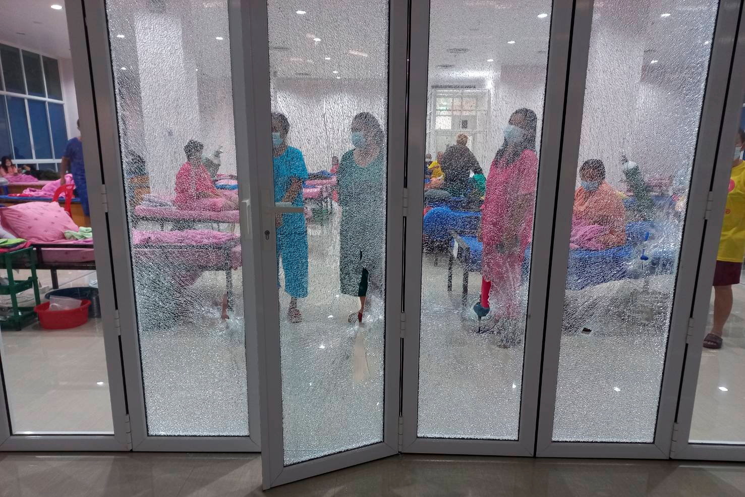 Patients are seen behind a broken glass door after a shooting in a coronavirus (COVID-19) field hospital in Pathum Thani, Thailand June 24, 2021. Dailynews via REUTERS  NO RESALES. NO ARCHIVES. THAILAND OUT. NO COMMERCIAL OR EDITORIAL SALES IN THAILAND