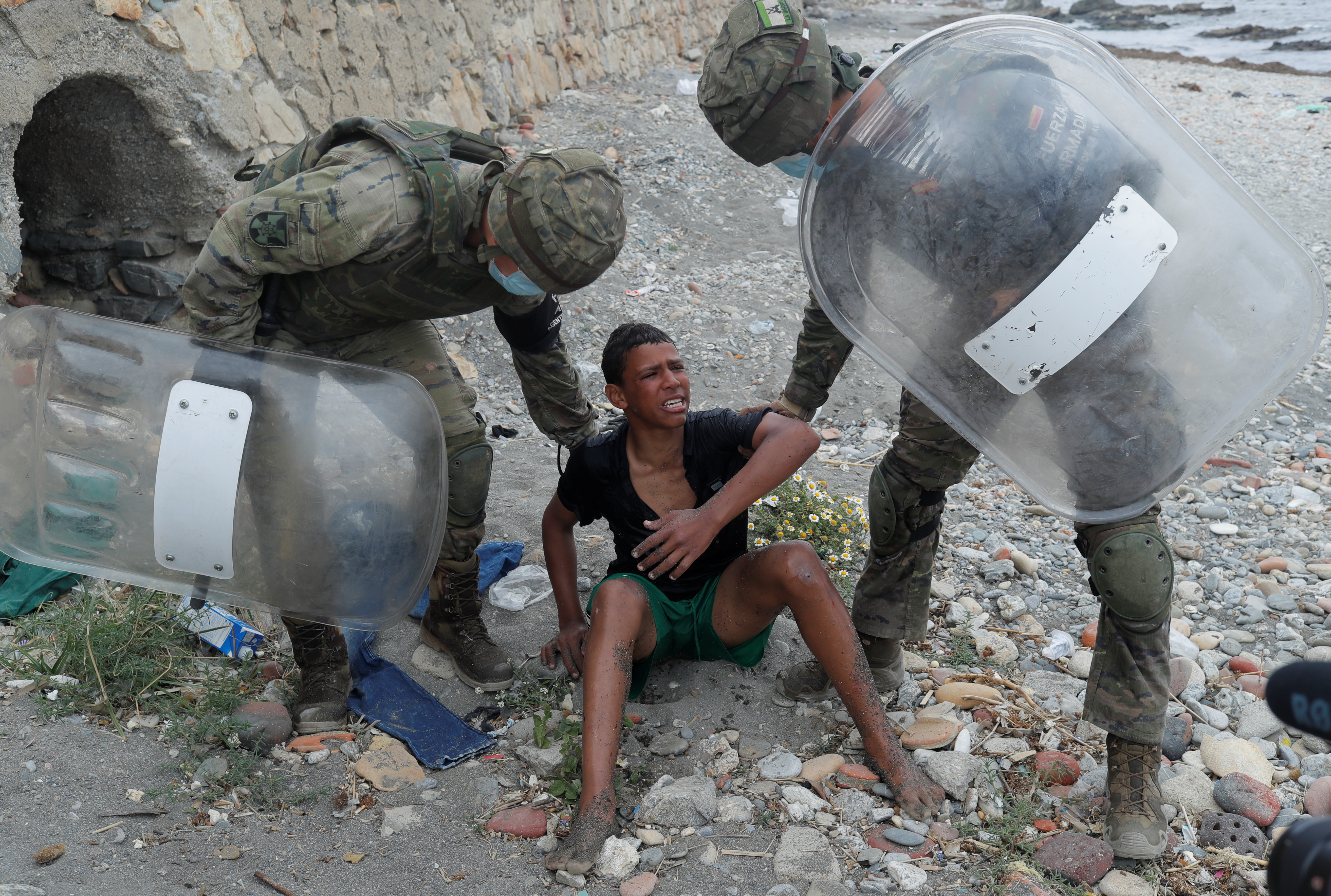 Spanish soldiers assist a migrant at El Tarajal beach, near the fence between the Spanish-Moroccan border, after thousands of migrants swam across the border, in Ceuta, Spain, May 19, 2021. REUTERS/Jon Nazca