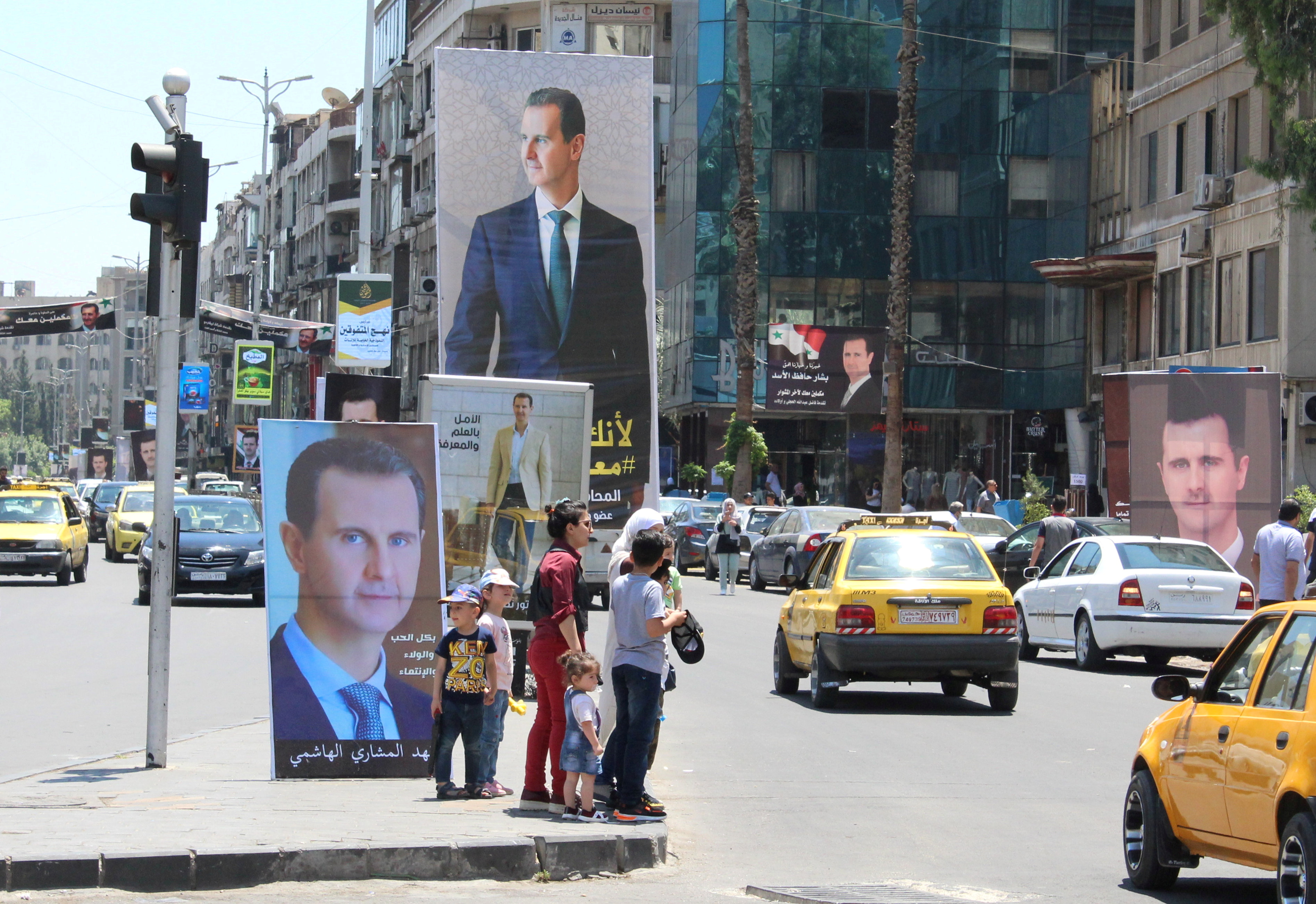 FILE PHOTO: People stand near posters depicting Syria's President Bashar al-Assad, ahead of the May 26 presidential election, in Damascus, Syria May 18, 2021. Picture taken May 18, 2021. REUTERS/Firas Makdesi/File Photo