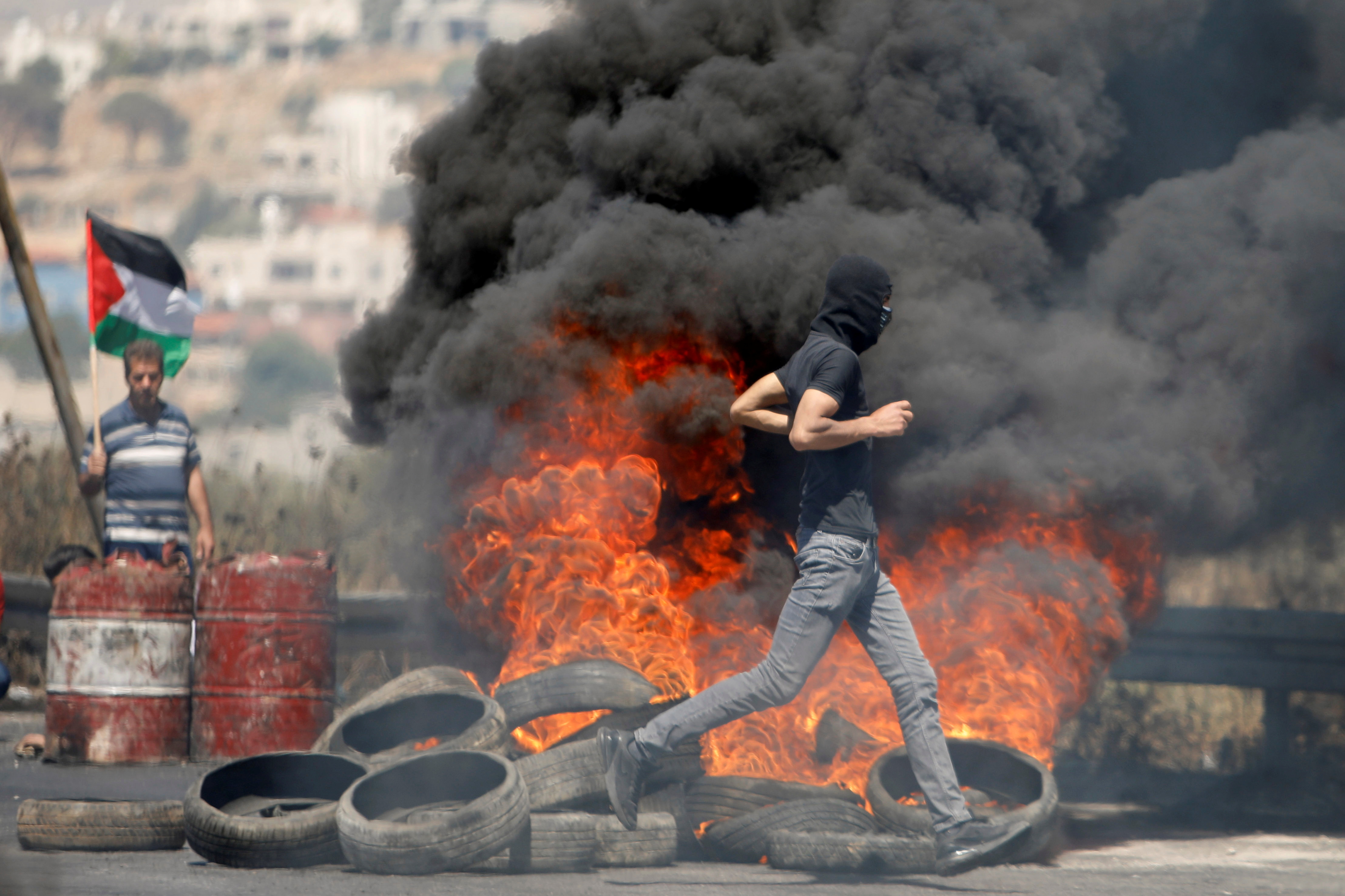 A Palestinian demonstrator runs past burning tires during a protest over tension in Jerusalem and Israel-Gaza escalation, near Hawara checkpoint near Nablus in the Israeli-occupied West Bank, May 14, 2021. REUTERS/Raneen Sawafta