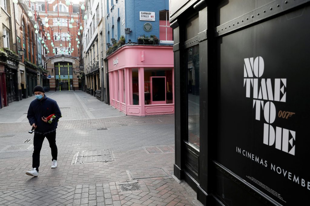 FILE PHOTO: A man wears a mask walking past a James Bond poster titled 'No Time To Die' at a near deserted Carnaby Street as the spread of the coronavirus disease (COVID-19) continues. London, Britain March 21, 2020 REUTERS/Peter Nicholls/File Photo