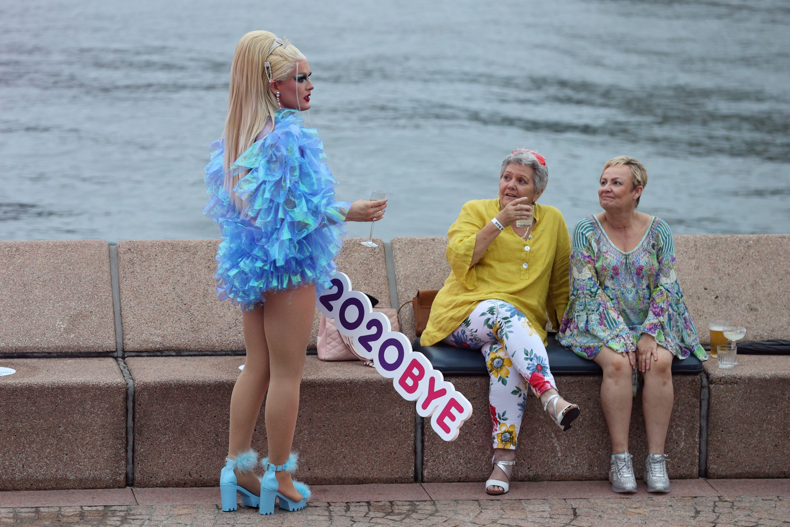 A reveller holds a sign reading "2020BYE" as a small number of people begin celebrating New Year's Eve at the Sydney Harbour waterfront amidst tightened COVID-19 prevention regulations in Sydney, Australia, December 31, 2020. REUTERS/Loren Elliott