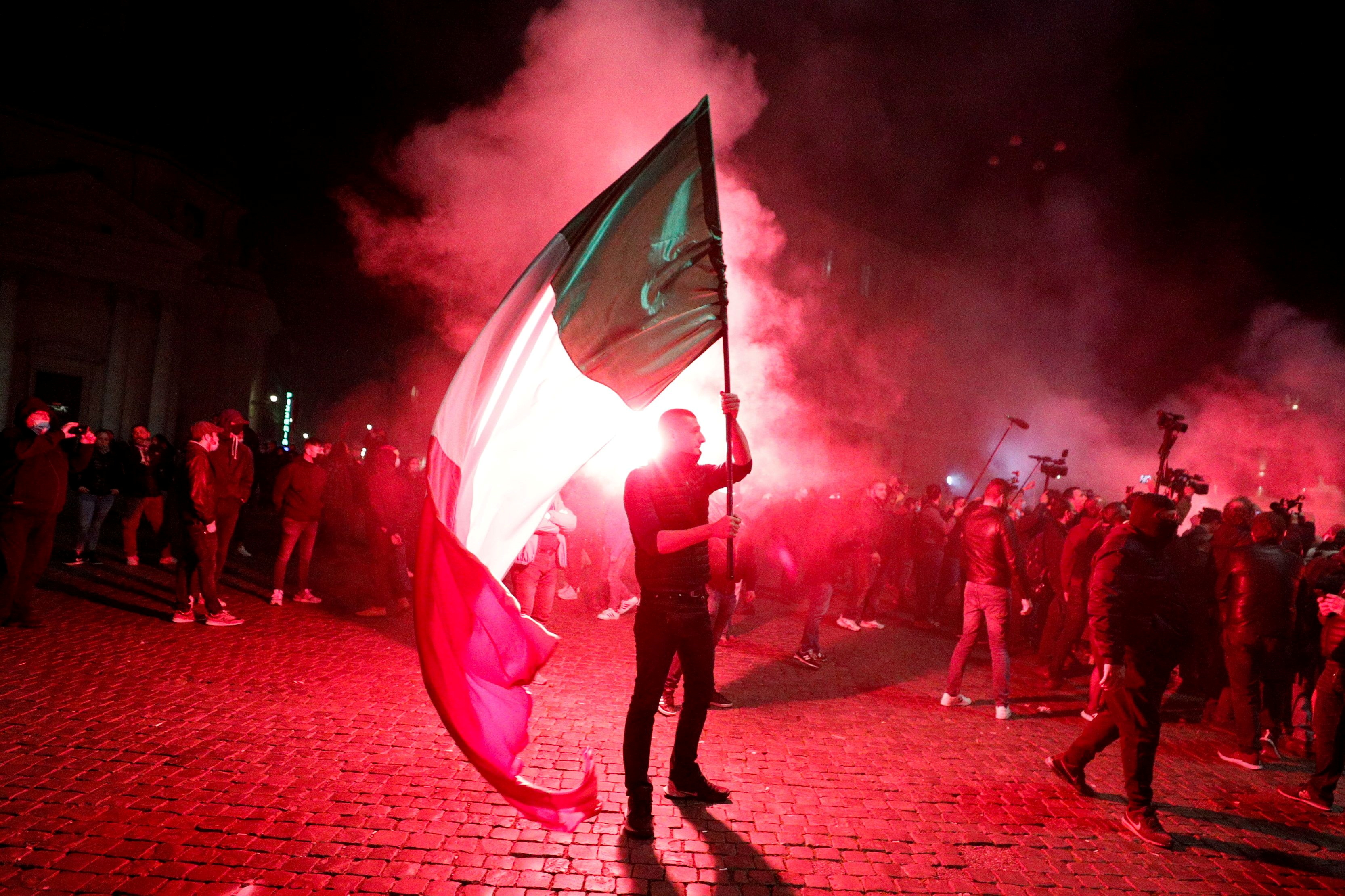 A far right demonstrator holds an Italian flag during a protest over the restrictions put in place to curb the coronavirus disease (COVID-19) infections in Rome, Italy October 27, 2020. REUTERS/Guglielmo Mangiapane     TPX IMAGES OF THE DAY