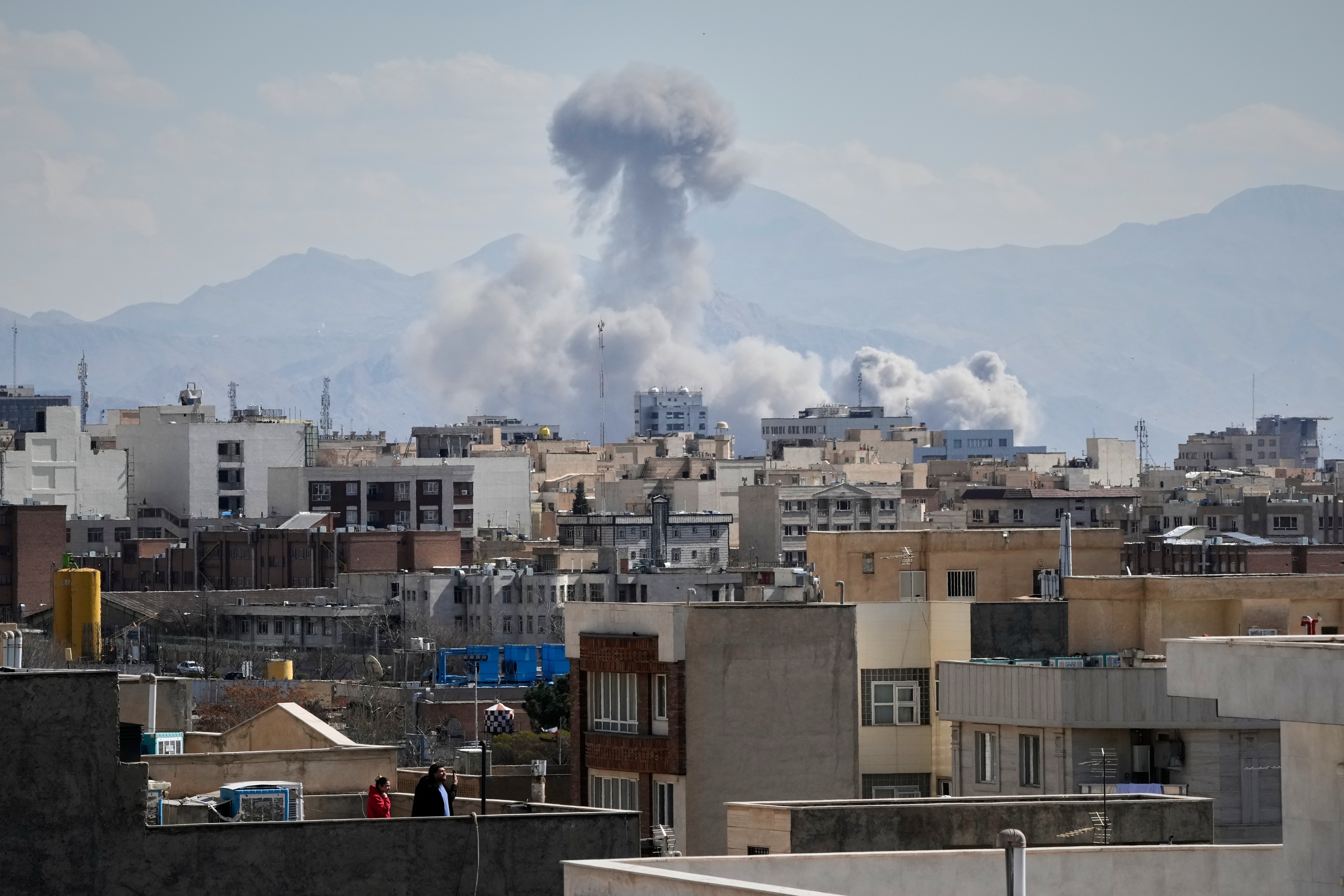 People watches from rooftop as a plume of smoke rises after a strike in Tehran, Iran, Sunday, March 1, 2026. (AP Photo/Vahid Salemi)