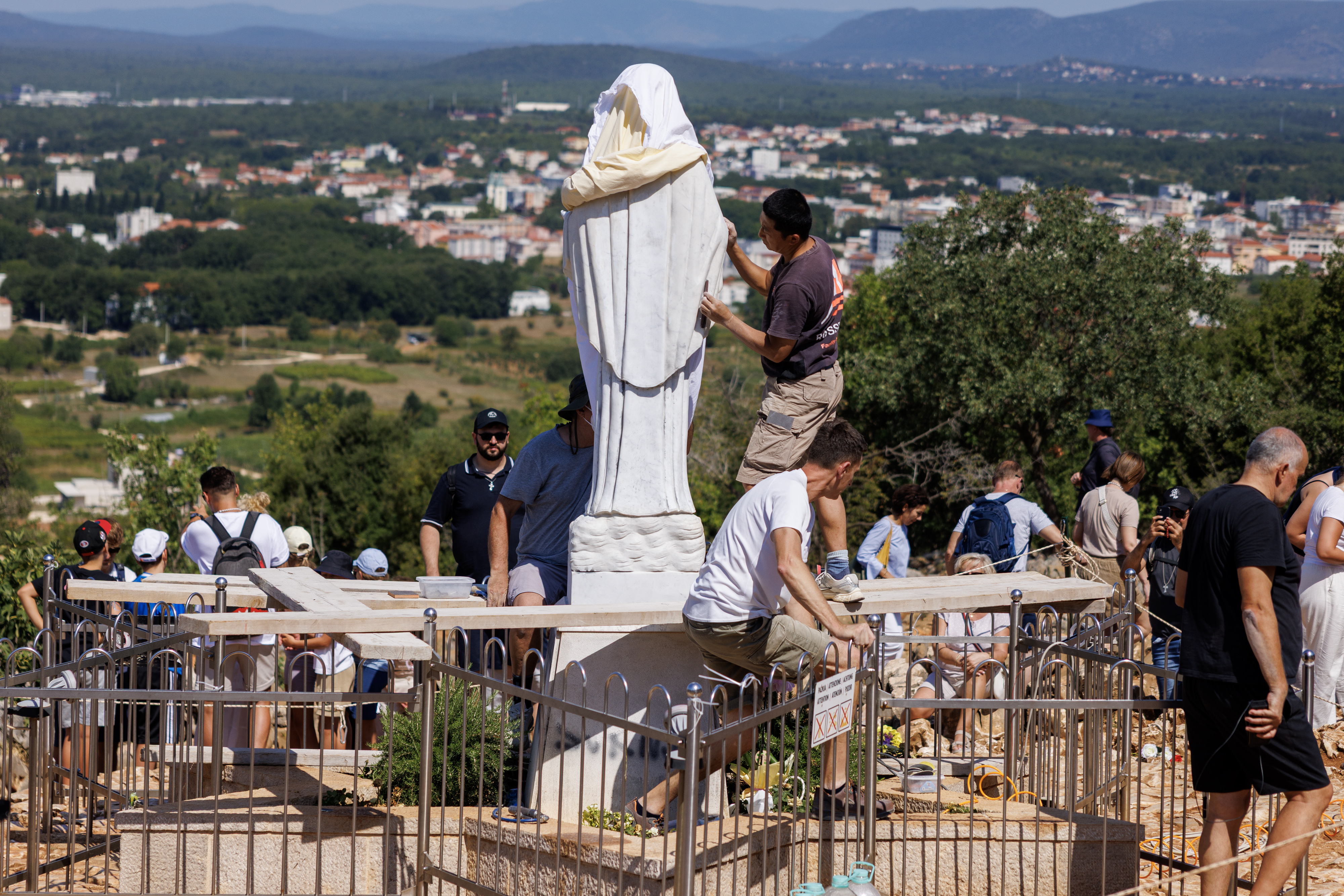 Volunteers clean the vandalized statue of the Virgin Mary, which has been covered with a white sheet, on Apparition Hill in Medjugorje, Bosnia, Tuesday, July 28, 2026. (AP Photo)
