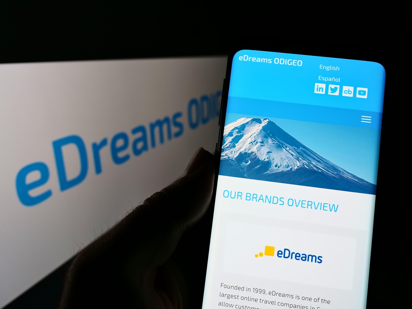 Person holding mobile phone with webpage of Spanish travel company eDreams ODIGEO SA on screen in front of logo. Focus on center of phone display.