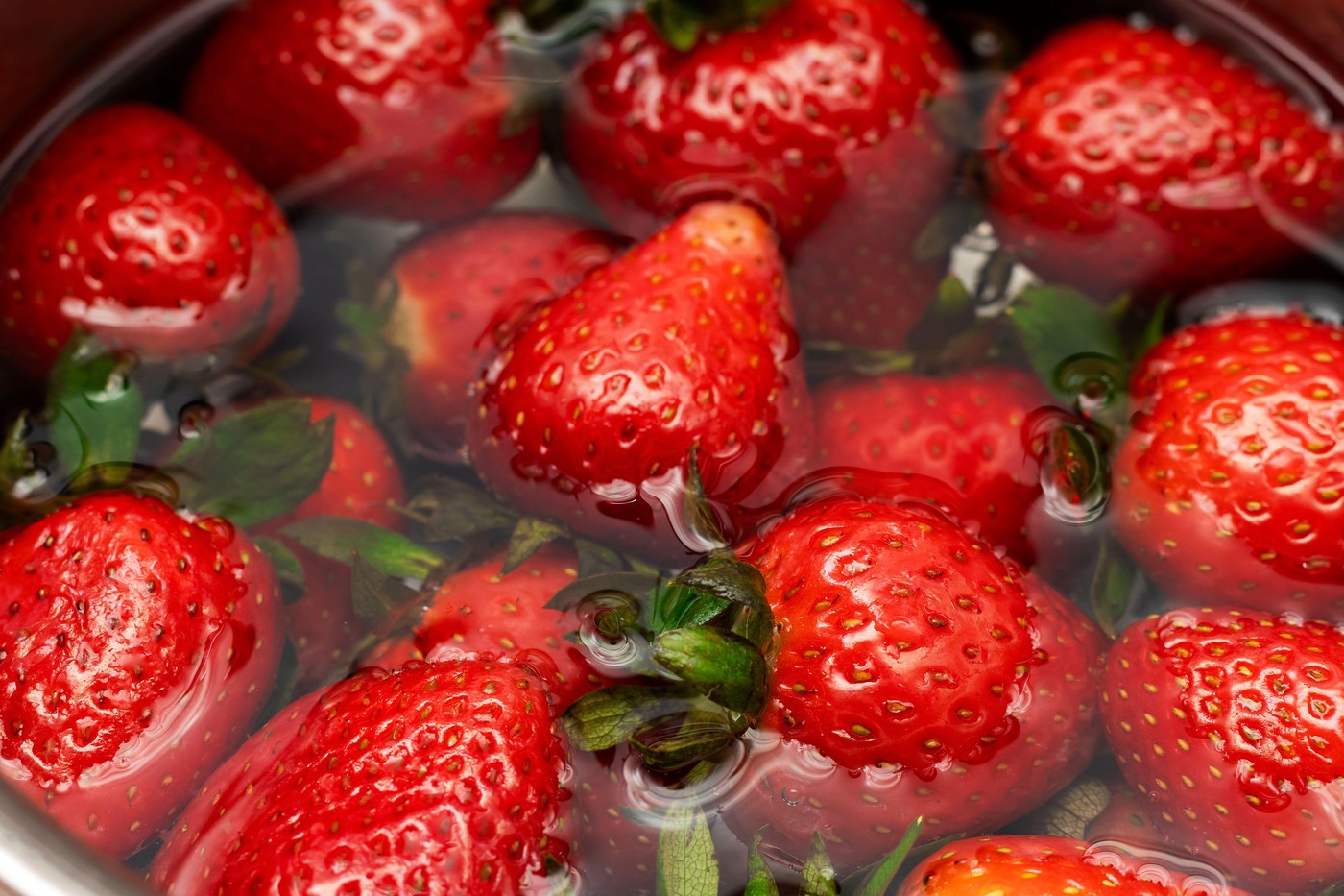 Close-up image of fresh, ripe strawberries being washed in clean water, highlighting their vibrant red color and juicy texture. The surface tension an