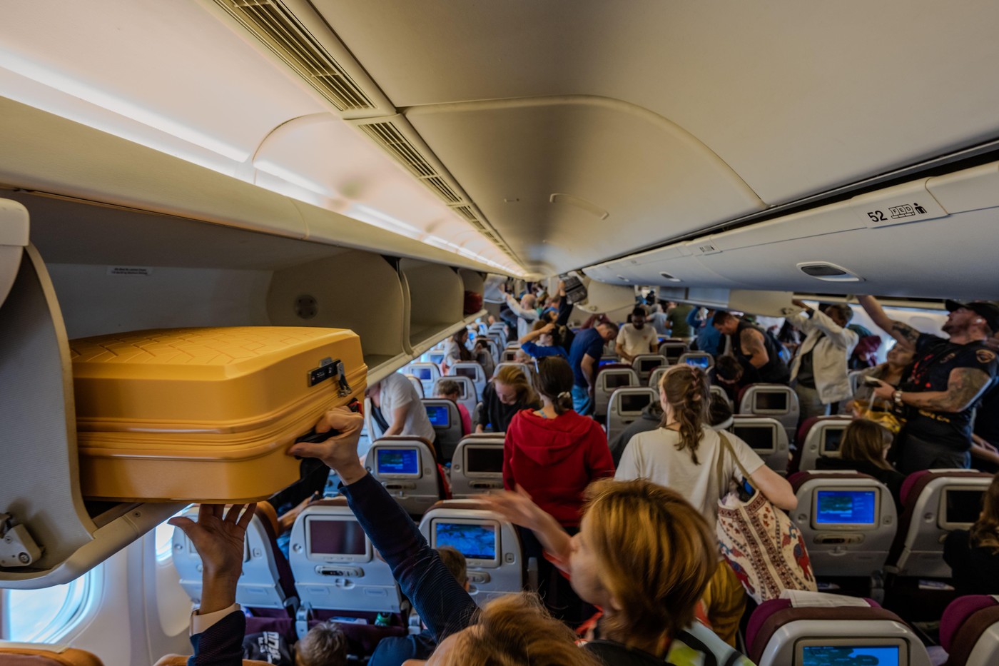 London, England - 10 July 2023, Passengers and Travelers Retrieve Luggage from Overhead Lockers While Waiting for the Airplane Door to Open After Land