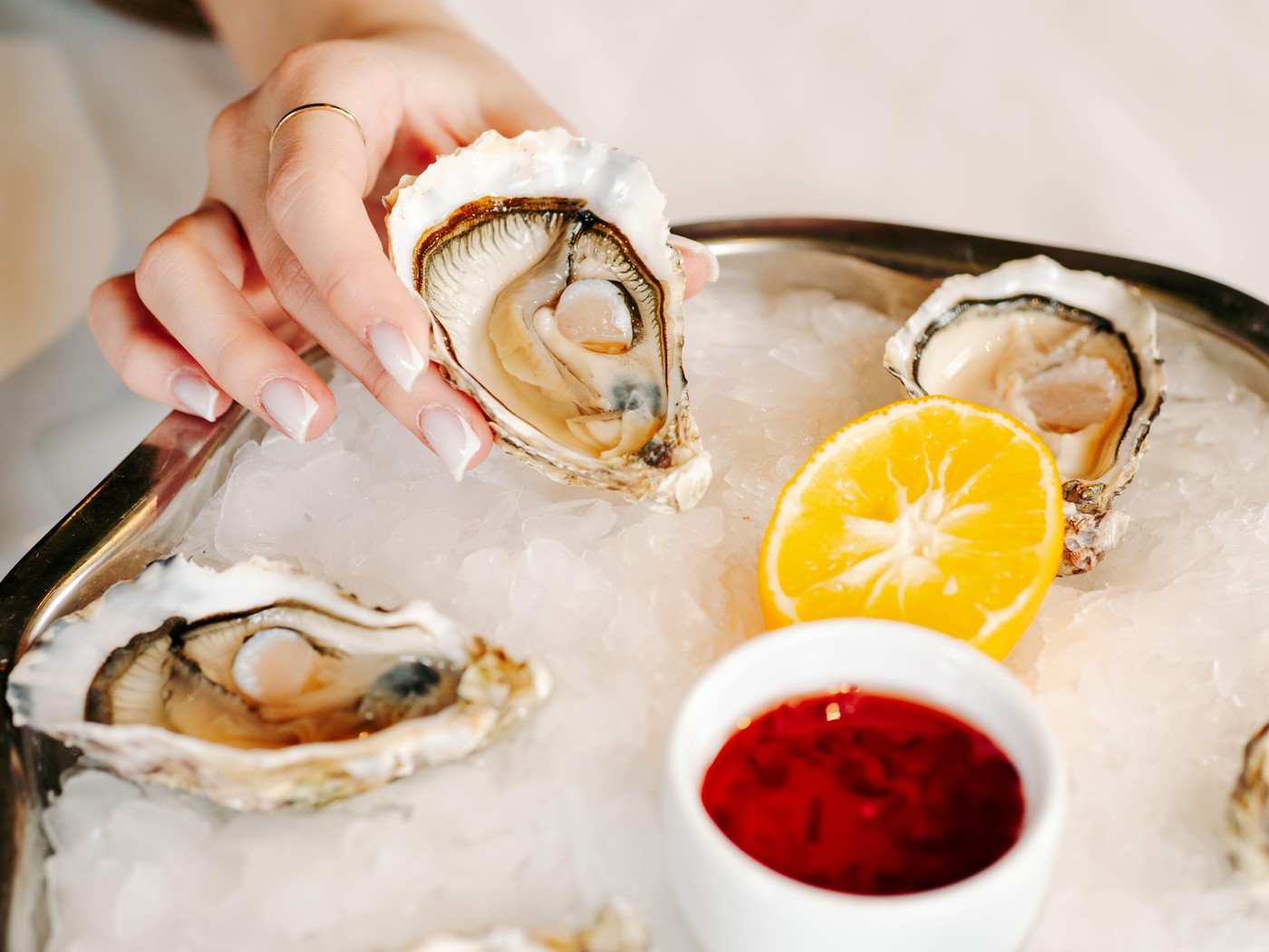 Woman having oysters at table. Fresh oysters on large plate with ice and lemon. Healthy food, gourmet food, restaurant food. Mediterranean cuisine, gi