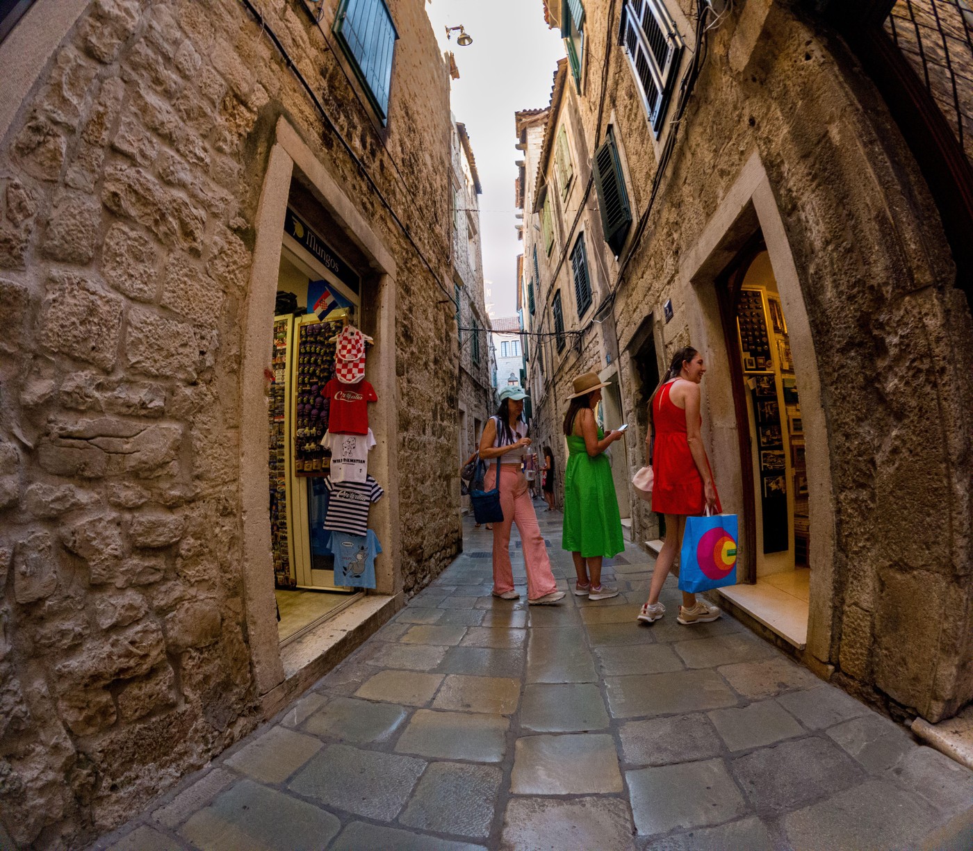 Split, Croatia - September 8th 2023: Three women are shopping in a narrow street. One woman is entering a shop with a shopping bag, while the others a