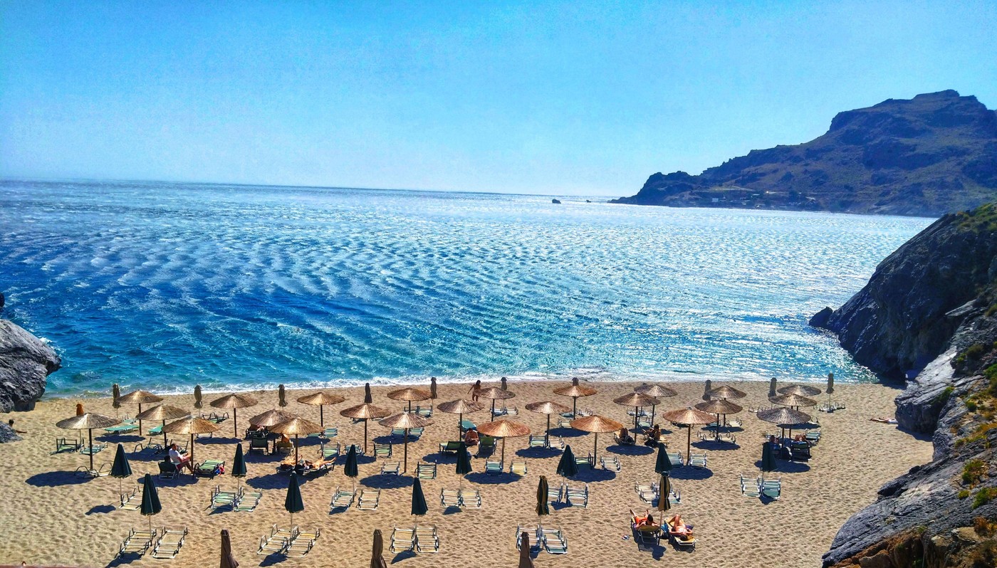 Rethymno, Crete, Greece – June 29, 2025: Organized beach with umbrellas and loungers, strong horizontal waves on the sea surface under bright sun.