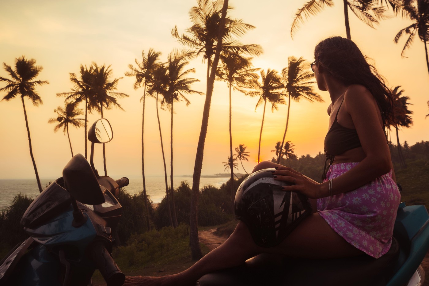 Carefree pretty woman on sit scooter by coastal viewpoint watch indian ocean and setting sun on sunset in Sri Lanka. Embracing freedom and romance whi