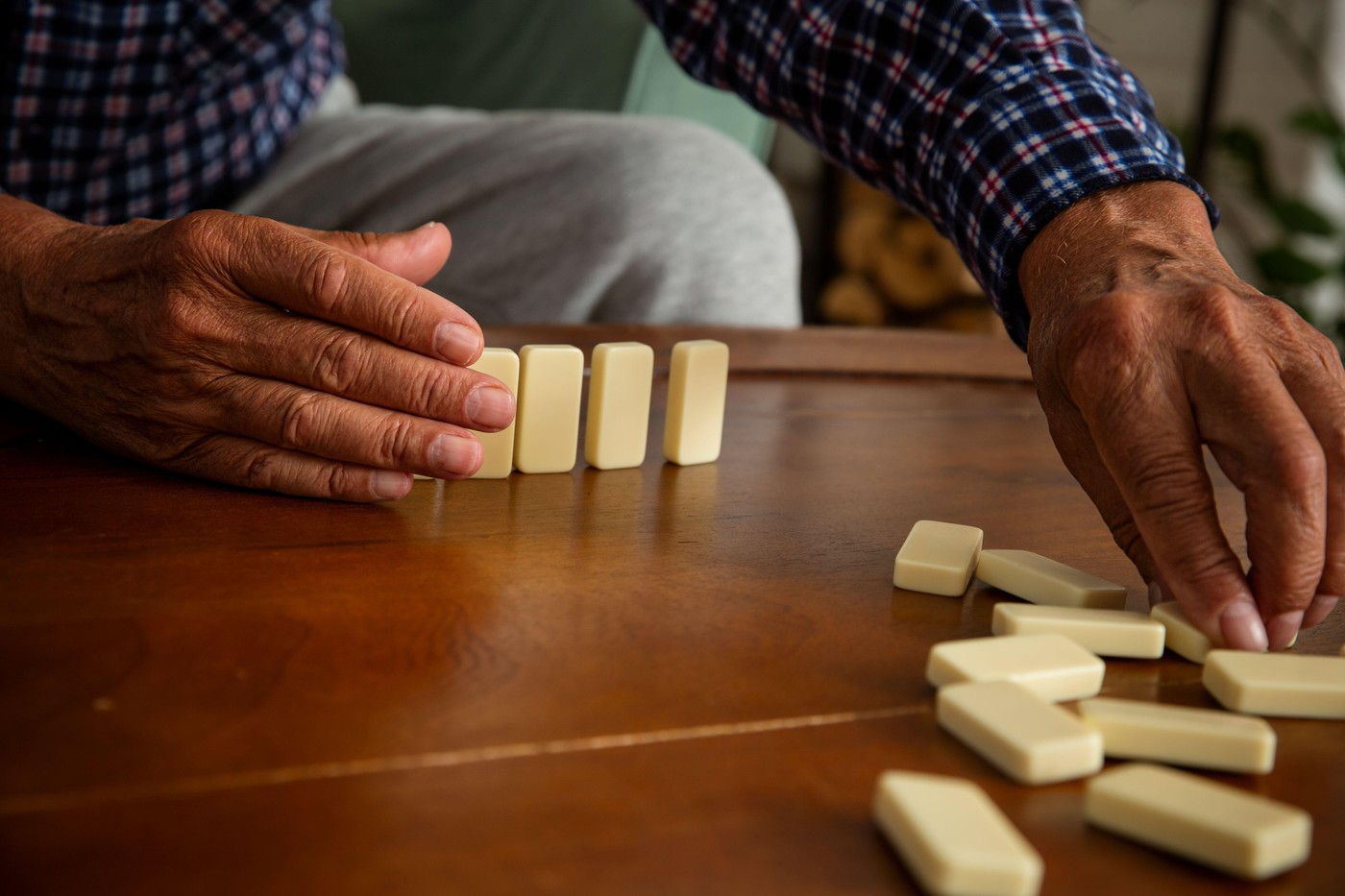 Close-up of elderly father's hands placing dominoes on the table during a quiet game with his adult son - a tender moment of age and connection.